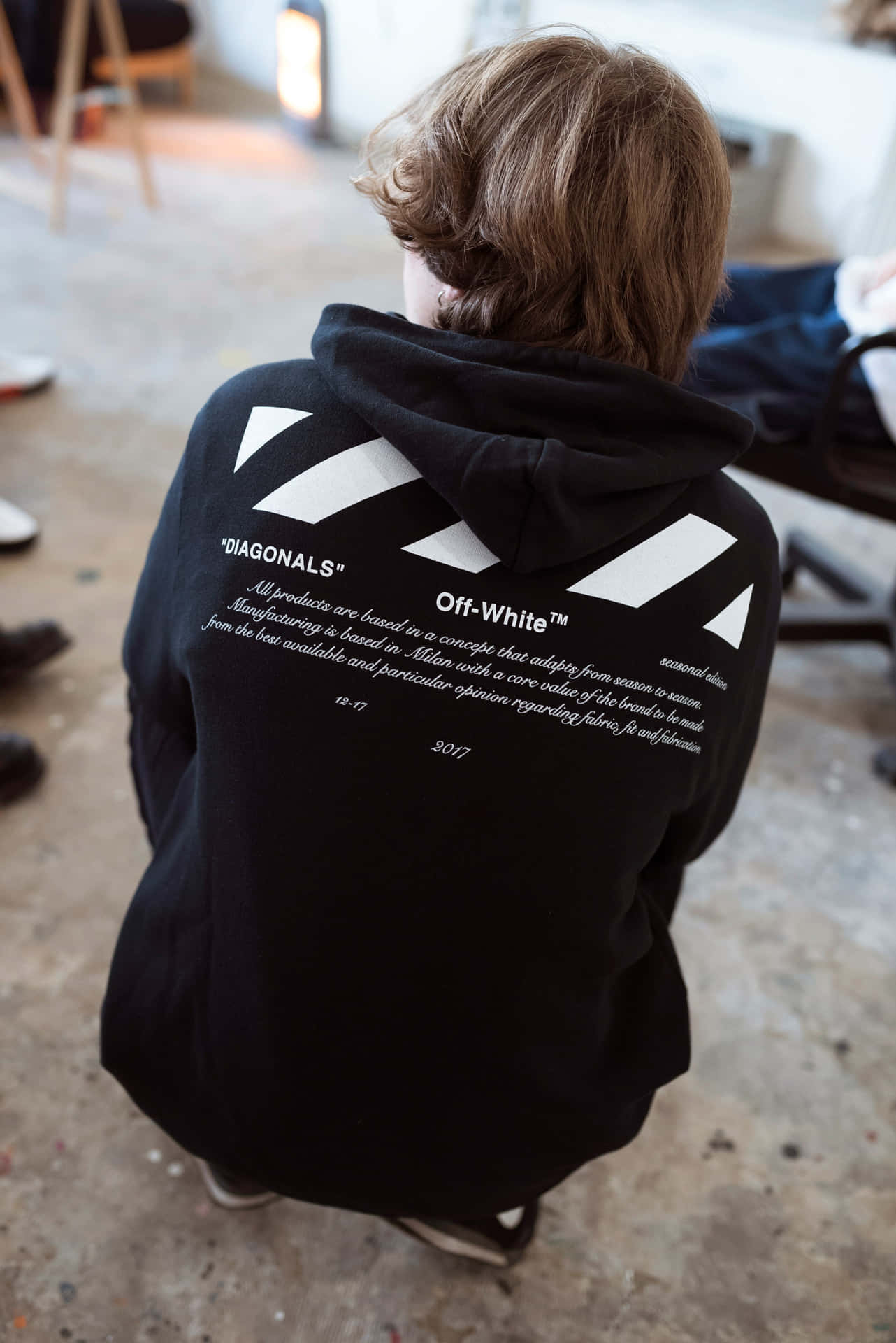 人穿著黑色 Off-White 連帽衫，帶有白色斜紋和文字。