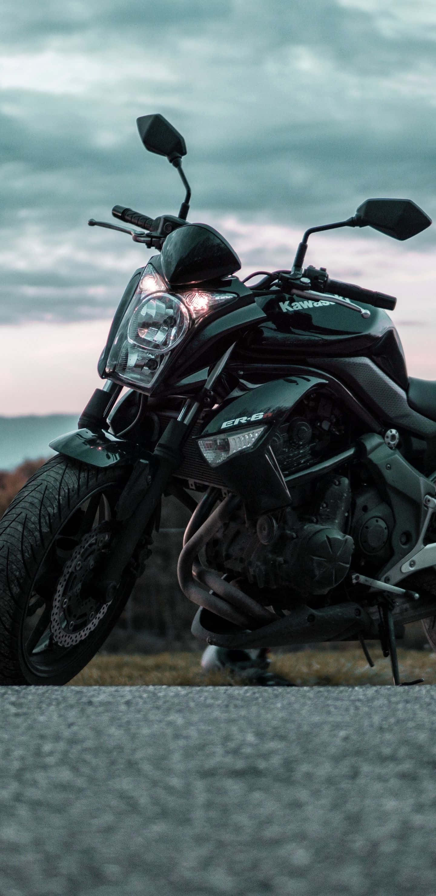以Pixel 3xl自行車點燃冒險熱情 壁紙 — 一架型格黑色Kawasaki ER-6電單車停泊在碎石路上，背景是帶有柔和粉紅與灰色雲層的憂鬱暮色天空。