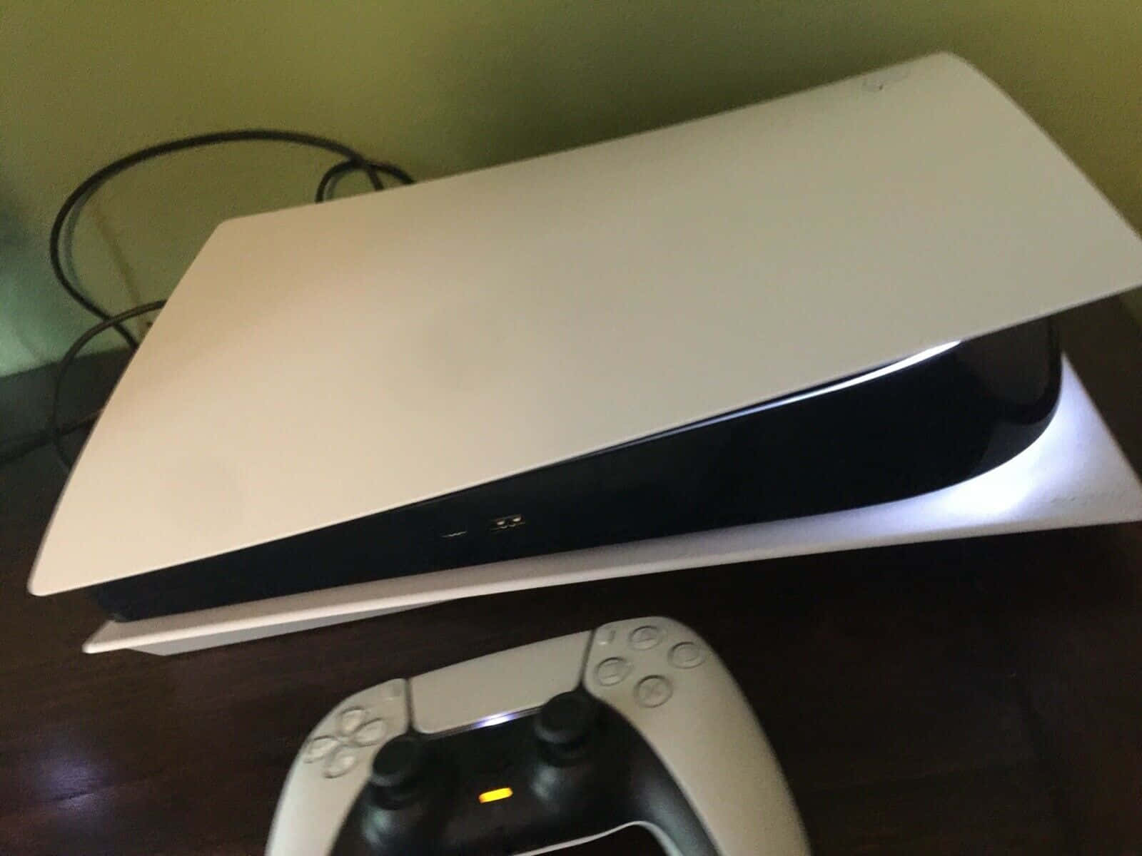 以PlayStation探索遊戲的下一層次 壁紙 — 一部白色PlayStation 5主機帶有發光燈光，放置在深色木質表面上，旁邊是其匹配的控制器。