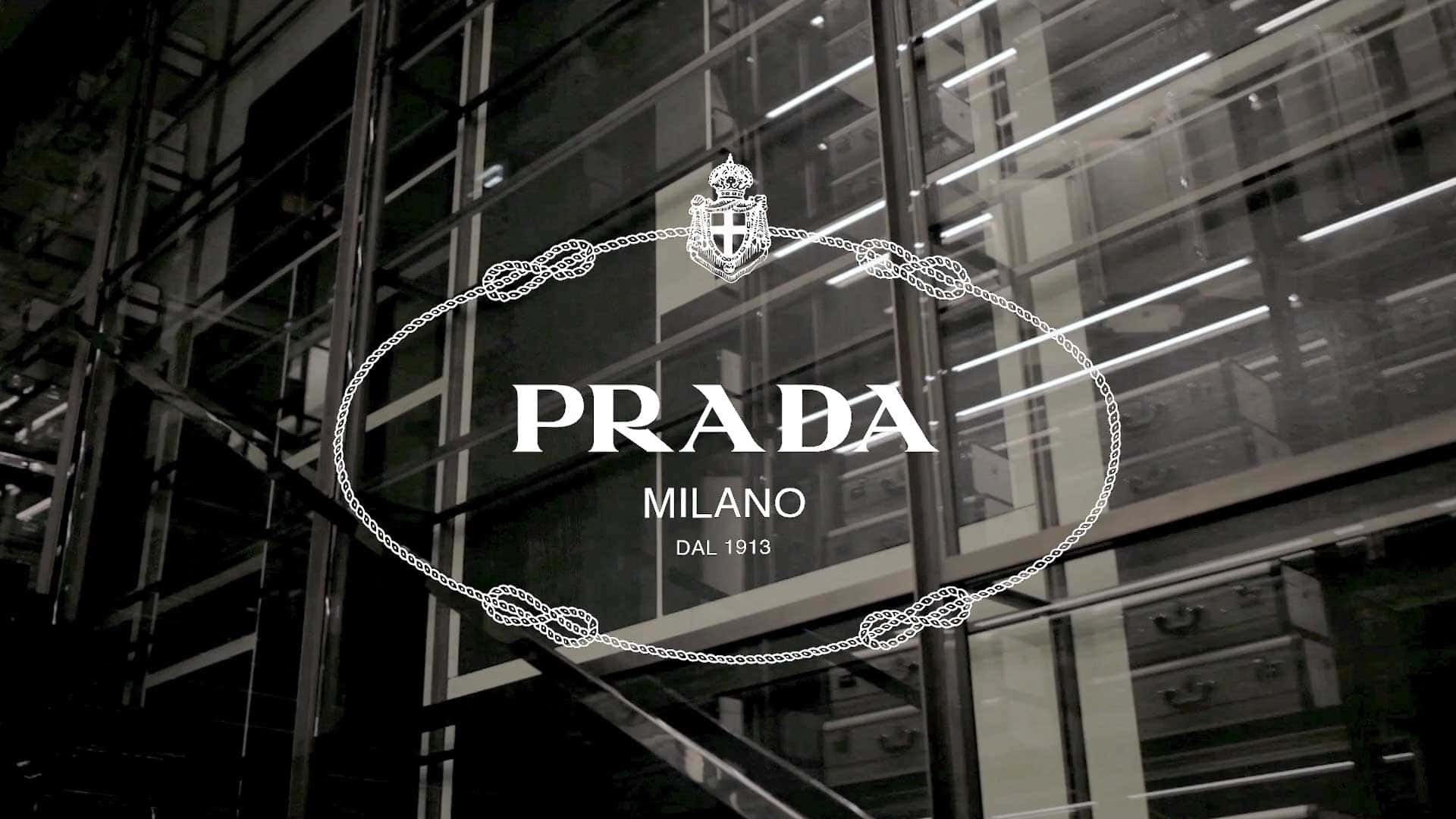 以Prada展現個人風格 壁紙 — 一個單色Prada商店標誌，帶有華麗的鏈條細節，在反射工業室內燈光的玻璃外牆上發光。