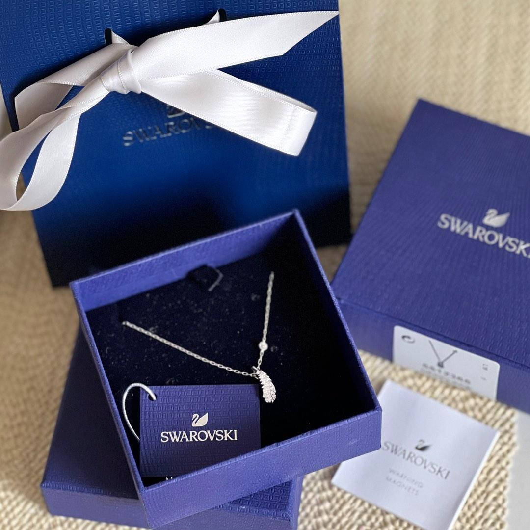 Swarovski羽毛項鍊放在藍色禮物盒中，配有白色絲帶，置於米色表面