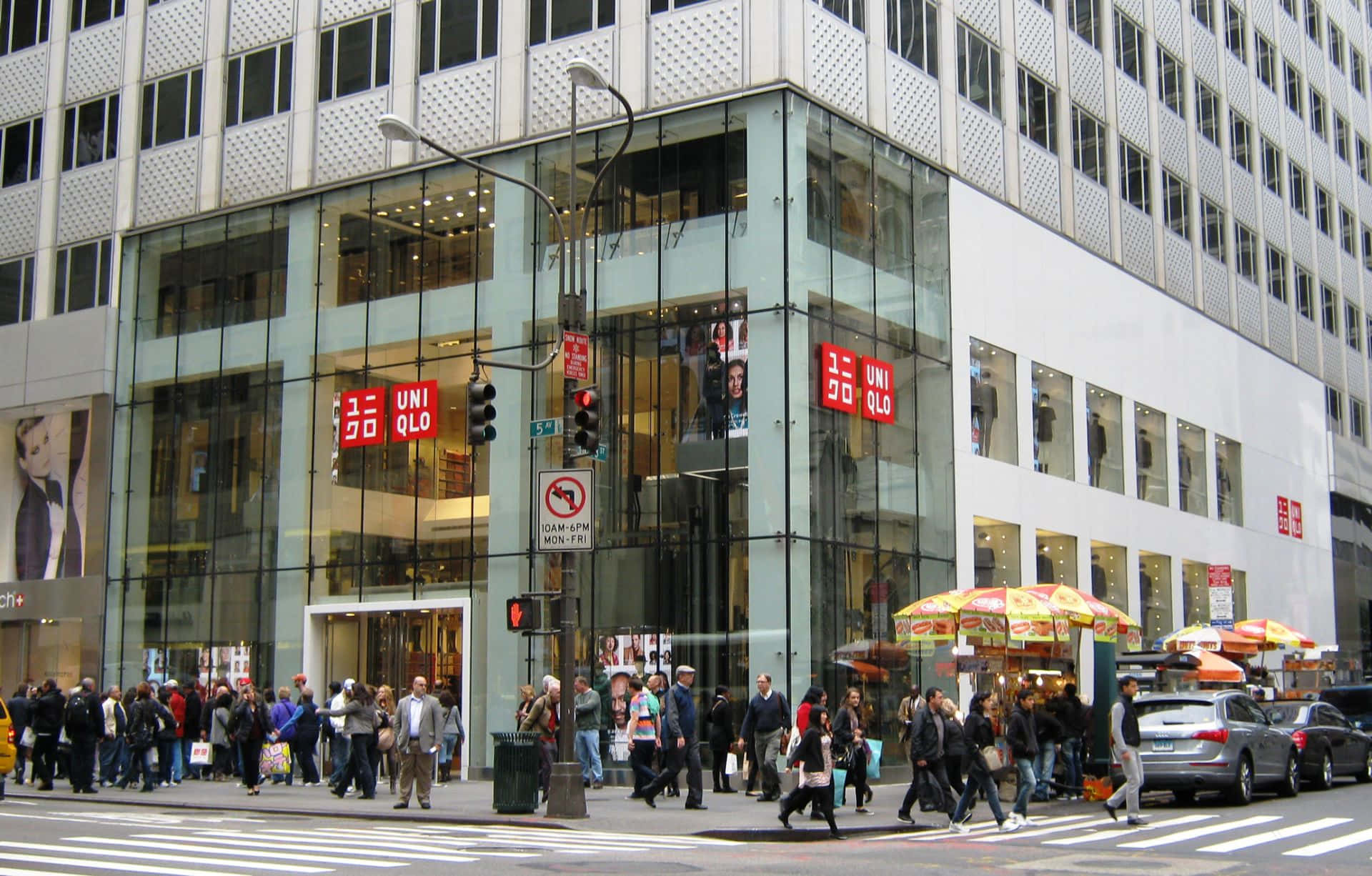 行人穿過城市街道，靠近帶有玻璃幕牆和紅色標誌的Uniqlo商店。
