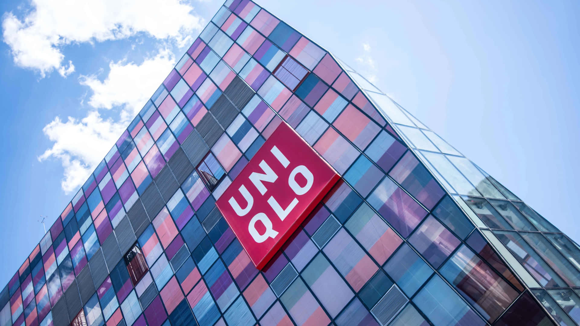 現代玻璃建築，彩色面板和UNIQLO標誌，藍天白雲下。
