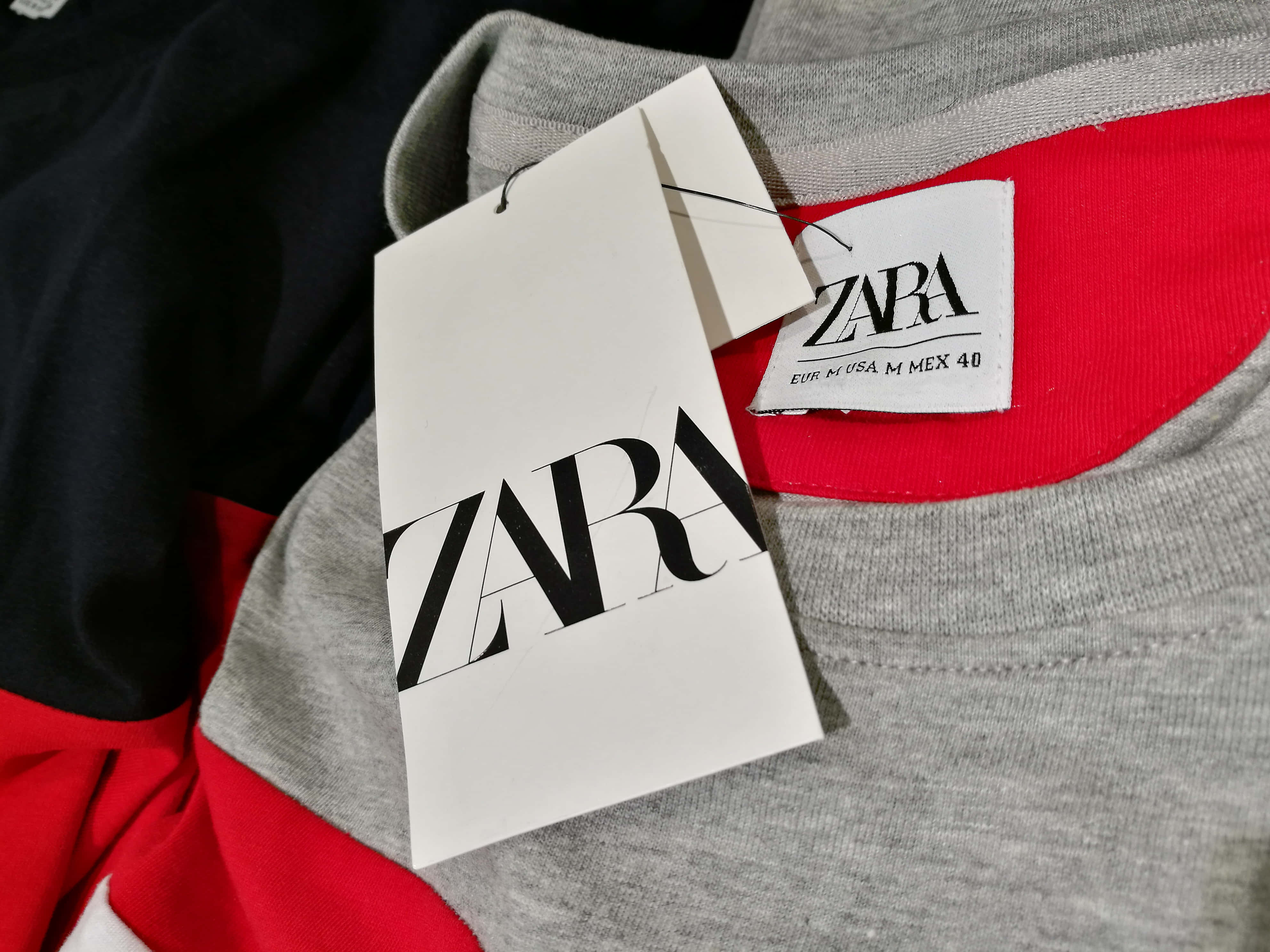 以Zara展現個人風格 壁紙 — Zara 服裝標籤的特寫，掛在帶有紅色點綴和尺寸標籤的灰色運動衫上。