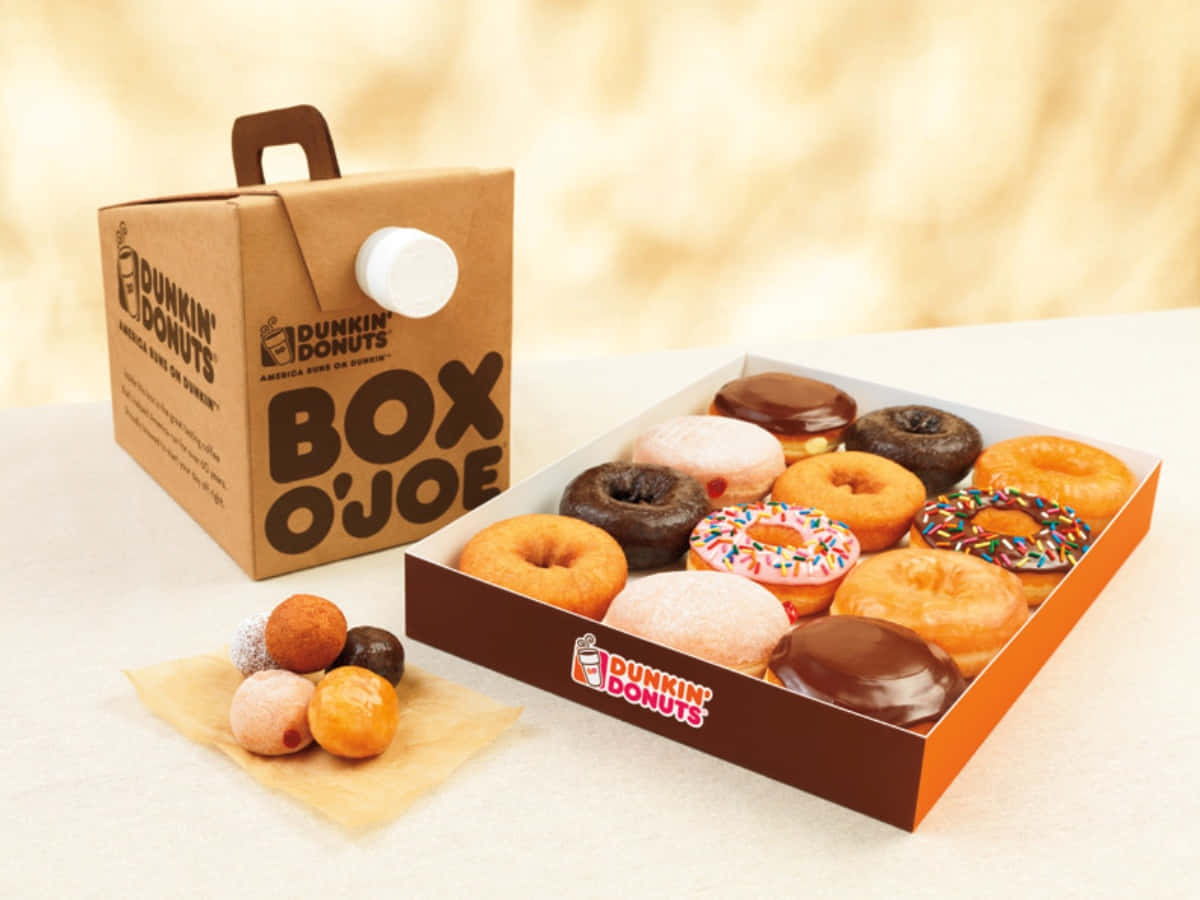 以一杯Dunkin' Donuts咖啡開始美好的一天 壁紙 — 一個Dunkin' Donuts Box O'Joe咖啡盒旁邊放著一盒各式各樣的糖霜和彩針甜甜圈，附近散落著迷你甜甜圈。