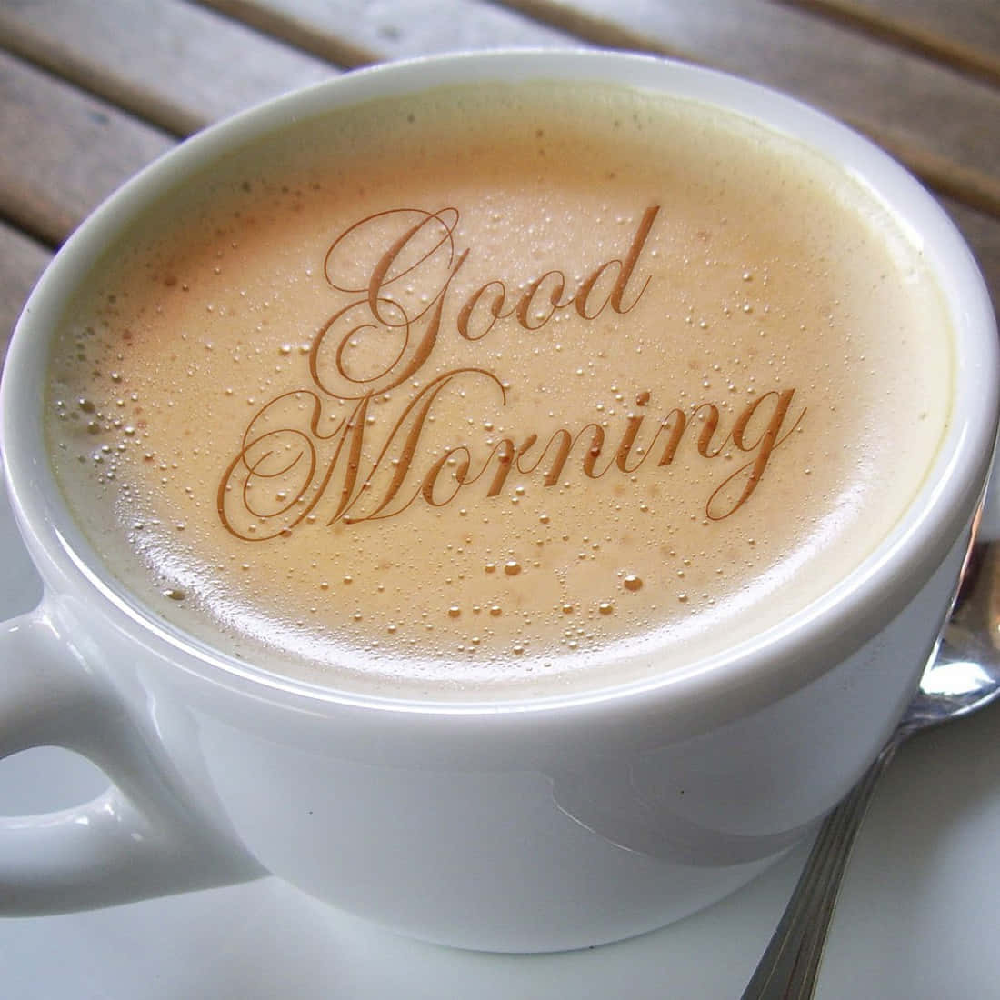 木桌上泡沫中寫有「Good Morning」的白色咖啡杯。