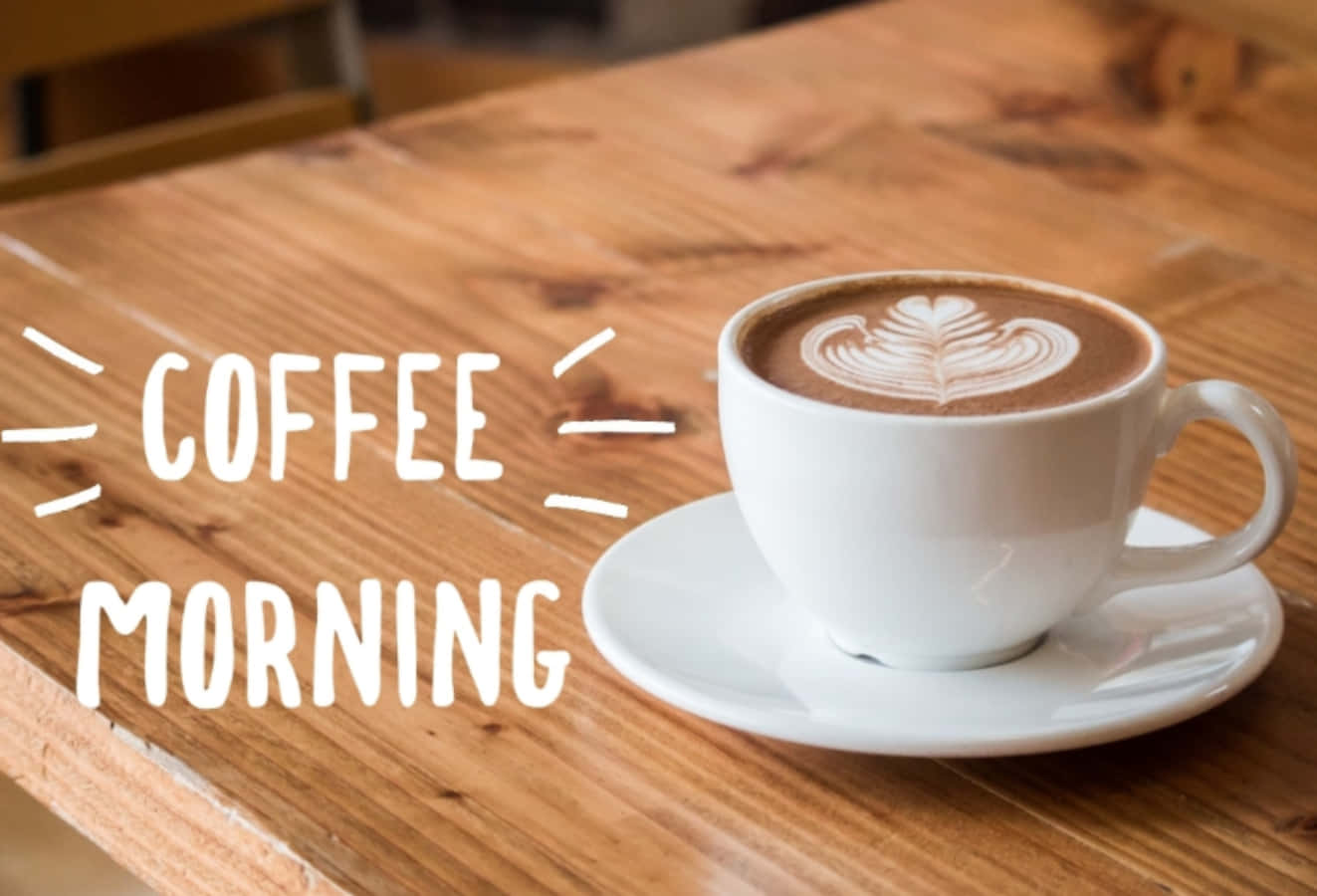 木桌上帶有葉子圖案的白咖啡杯，附有 coffee morning 文字。