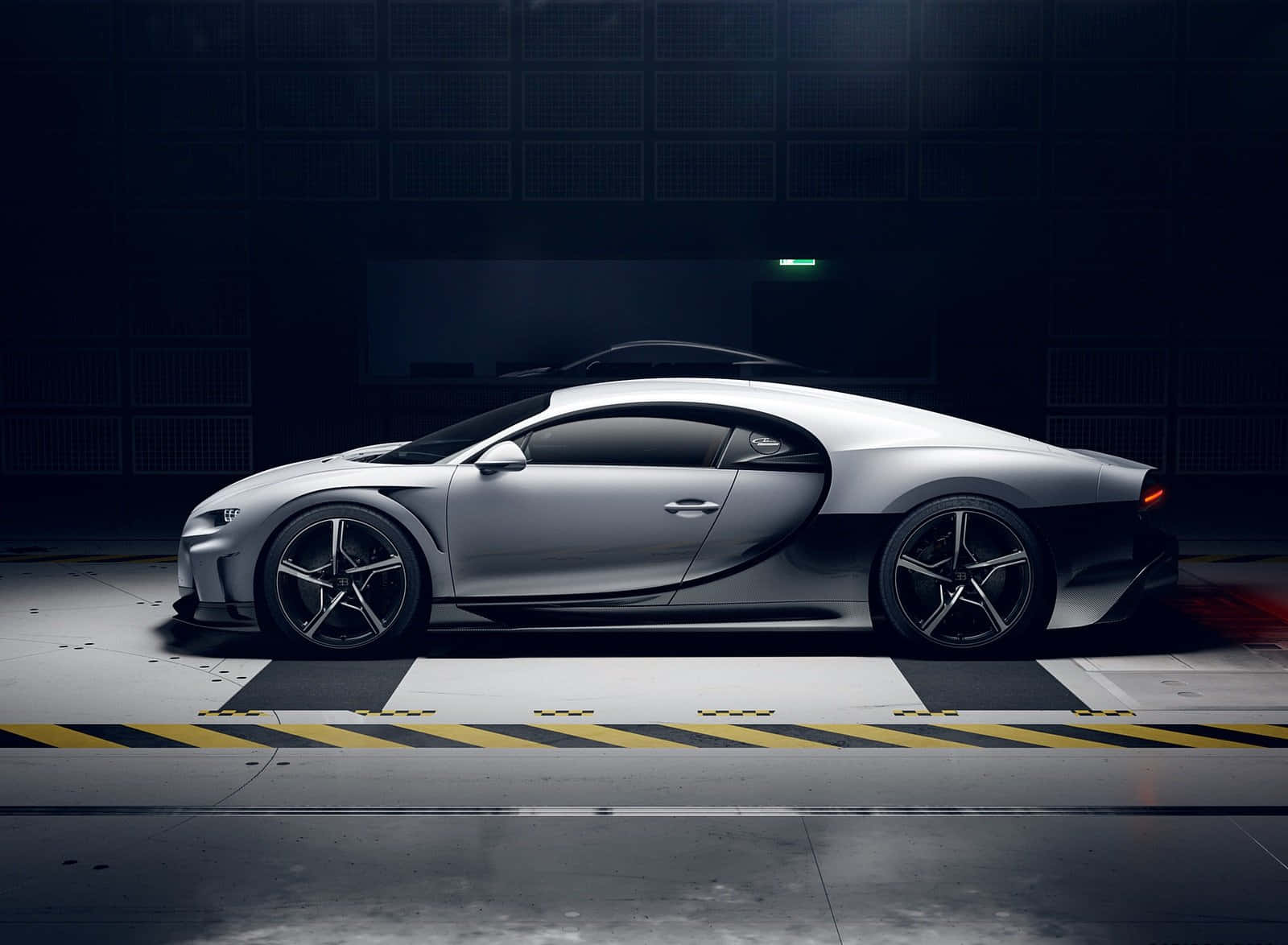 銀色Bugatti超跑在黑暗的工業車庫中，地面有黃色條紋。