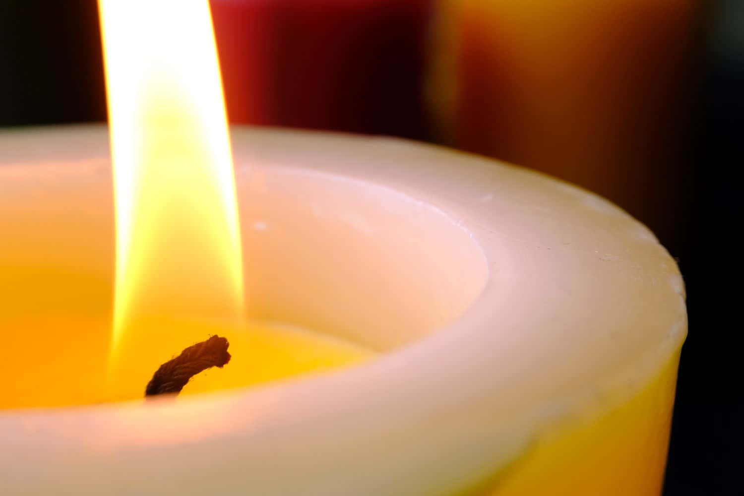 以優雅蠟燭點亮你的空間 壁紙 — 一支點燃的白色蠟燭的特寫，明亮的黃色火焰在蠟燭表面投射出溫暖的光芒。