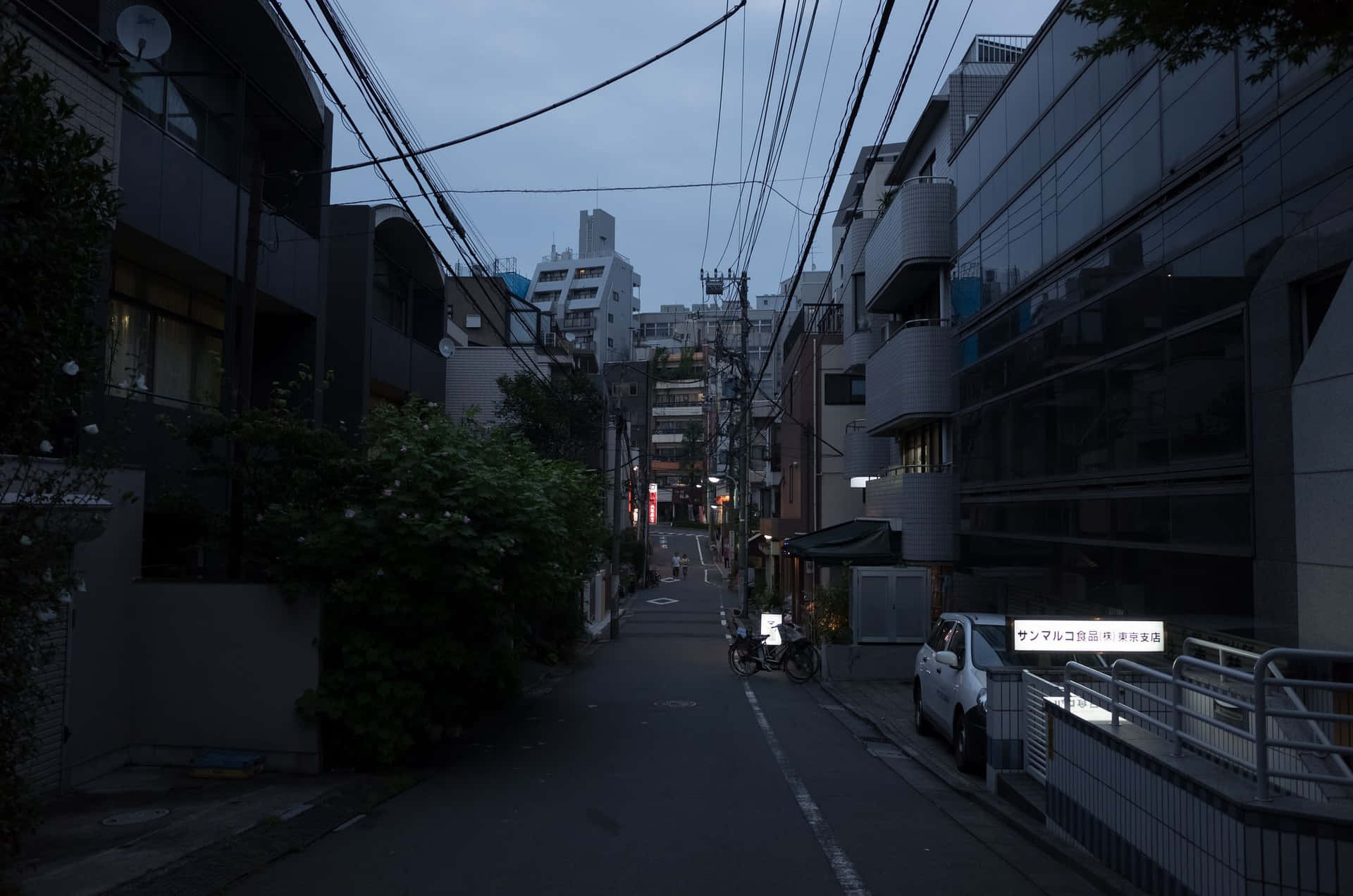 黃昏時分燈光昏暗的城市小巷，停放的汽車和現代建築。