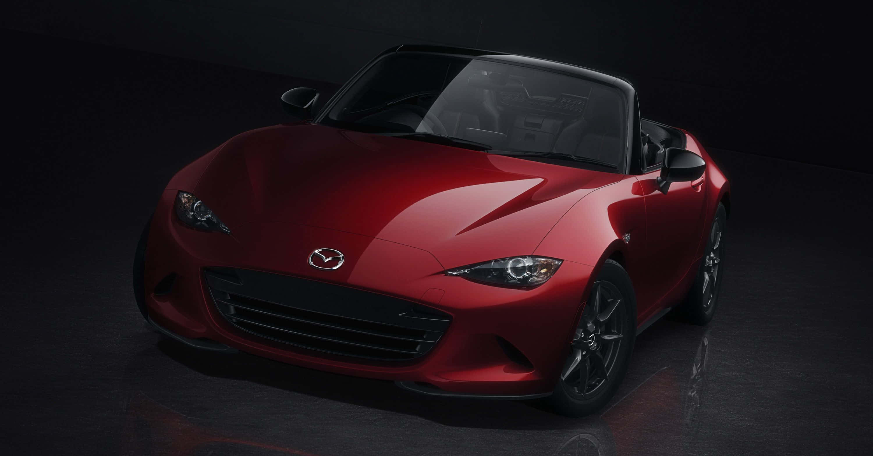 以全新馬自達MX-5 Miata加速你的夏日時光 壁紙 — 一輛光亮的紅色Mazda MX-5 Miata敞篷跑車在攝影棚燈光下，在深色反光地板上閃閃發光。