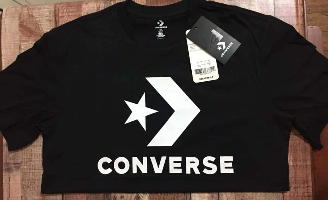 以創意Converse鞋履留下難忘印象 壁紙 — 一件黑色短版Converse T恤，帶有白色標誌，平放在木質表面上，標籤仍附著。
