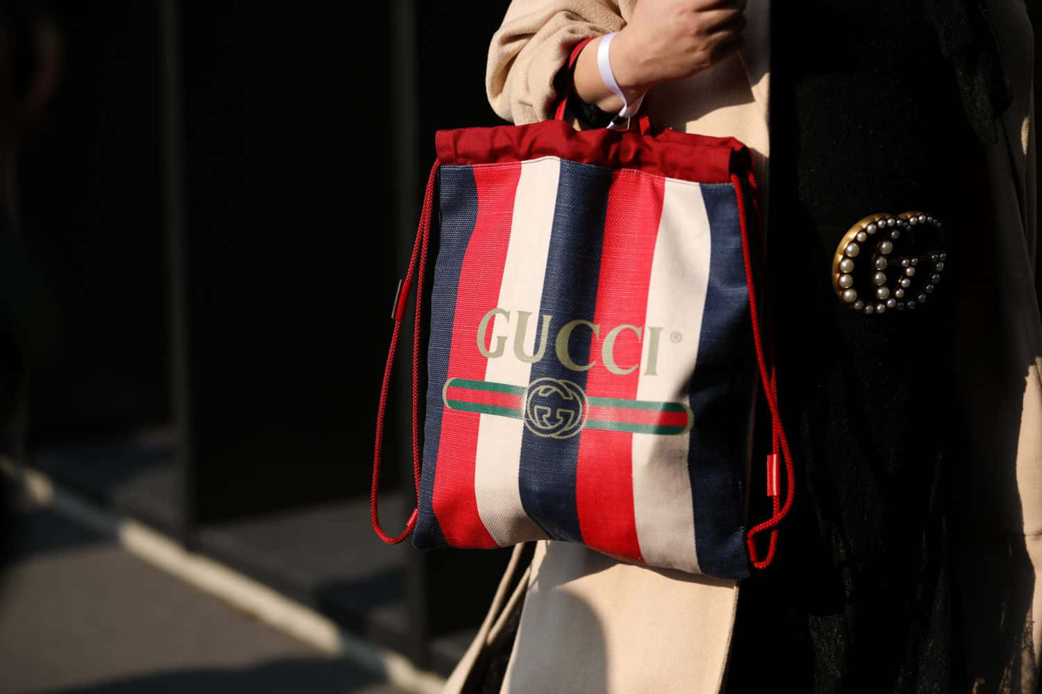 喺城市環境中，一個人拎住Gucci間條束繩袋。