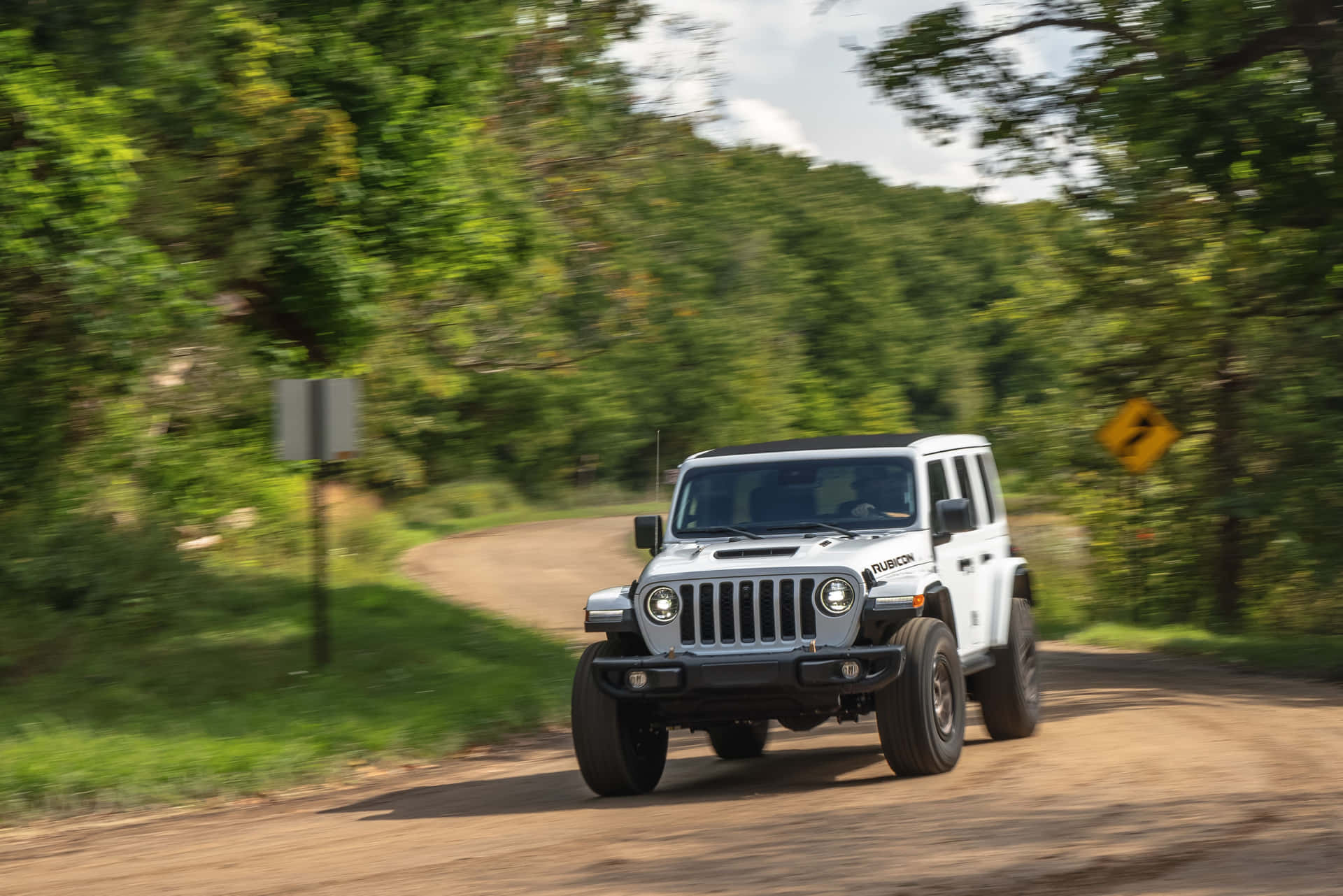 白色Jeep Wrangler在森林泥路上快速行駛。