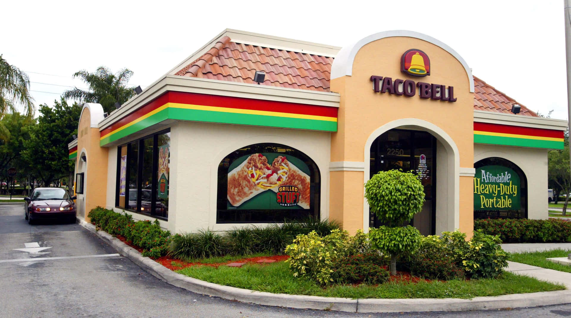 Taco Bell餐廳，米色牆壁和紅色瓦片屋頂，周圍環繞著綠色植物。