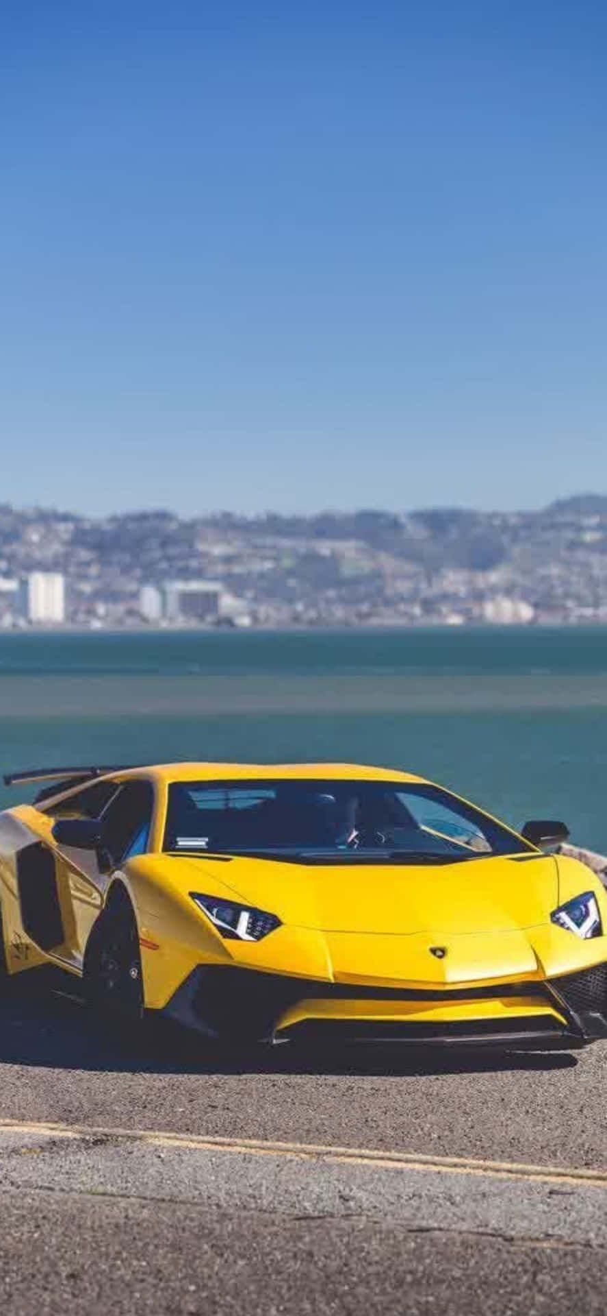 黃色林寶堅尼Aventador停泊在海邊，遠處有城市。