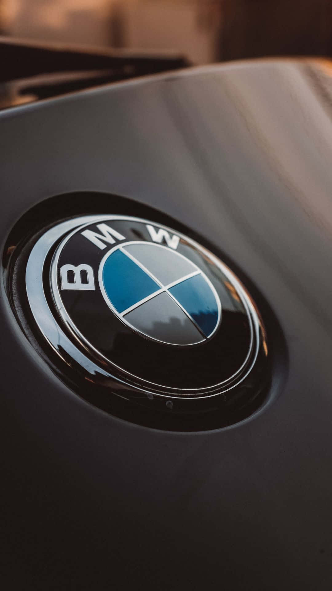 以安卓掌控您的BMW 壁紙 — 近距離拍攝亮黑色BMW標誌，在流線型引擎蓋上反射溫暖環境光。