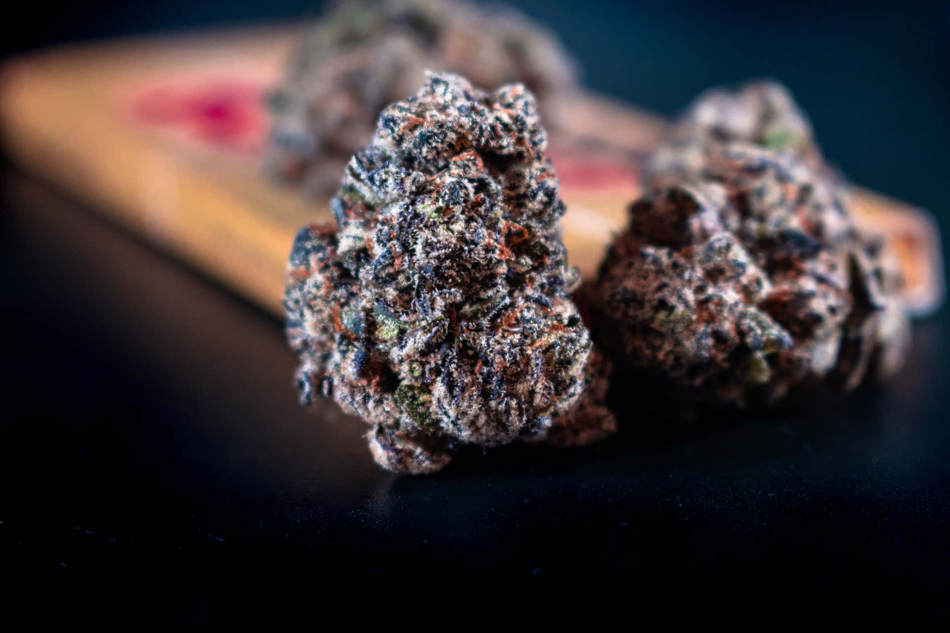 三個帶有霜狀毛狀體的大麻花蕾在深色表面上。