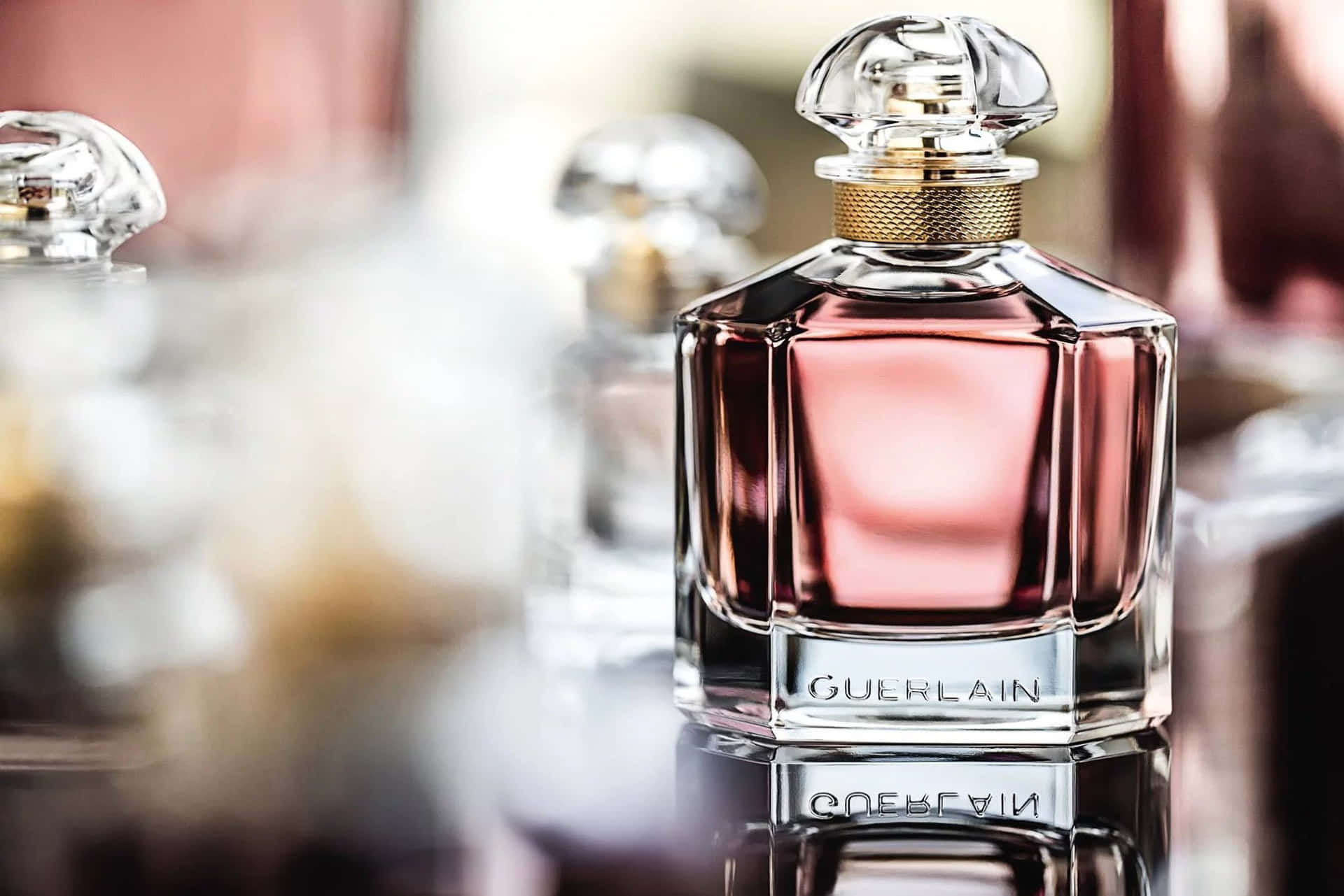 Guerlain 香水瓶，帶有粉紅色液體和水晶瓶塞，置於反光表面。