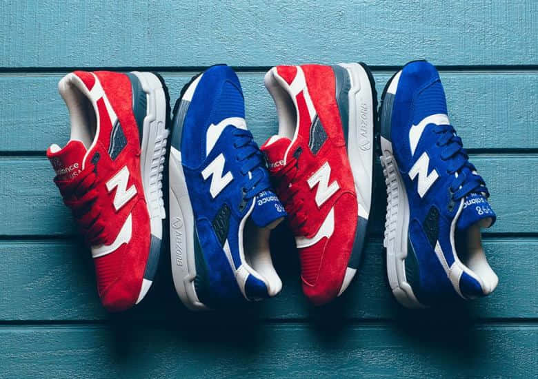 四雙紅色和藍色的New Balance運動鞋排列在青綠色木頭上。