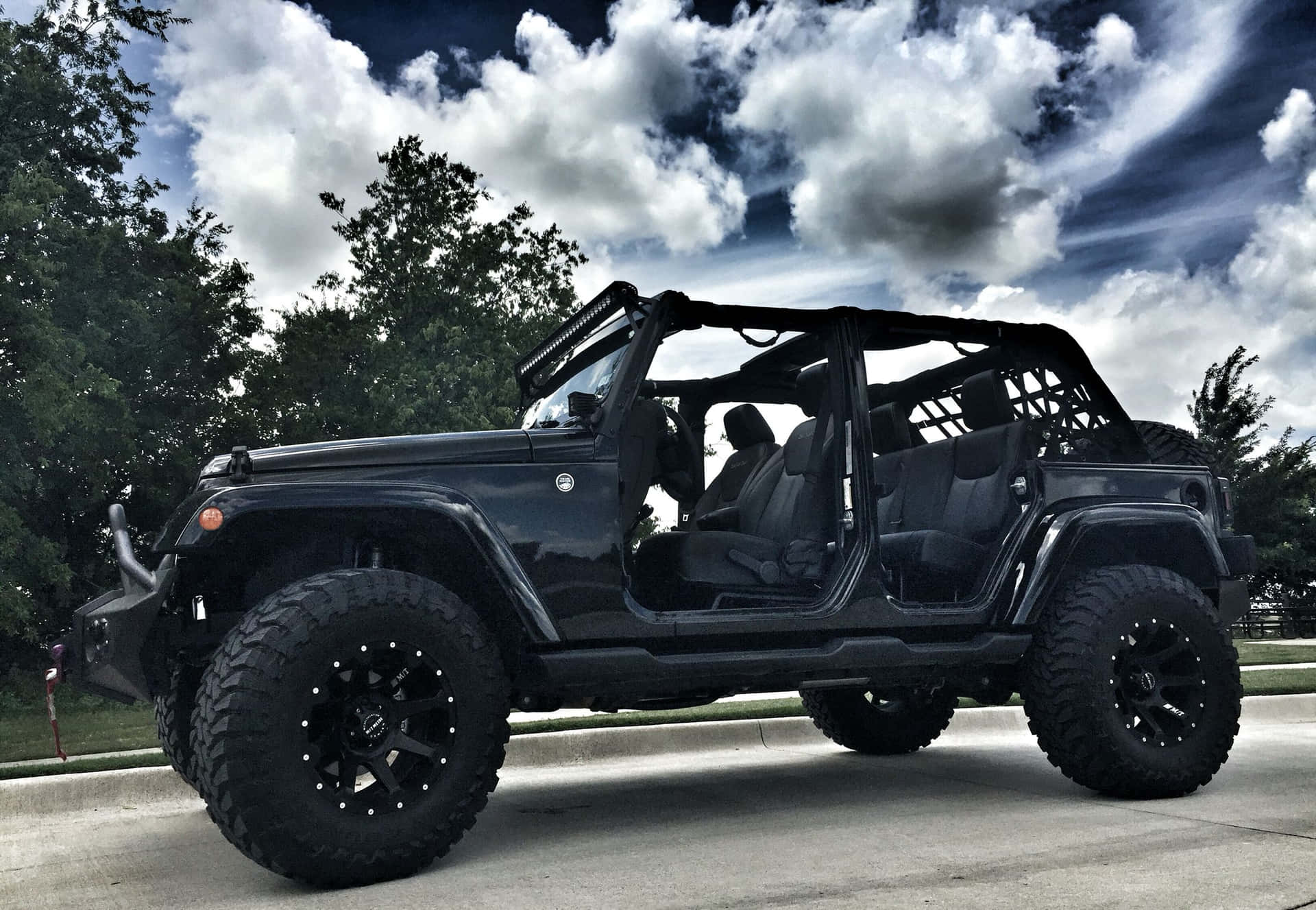 黑色Jeep Wrangler車門打開，停在有樹木和多雲天空的車道上。