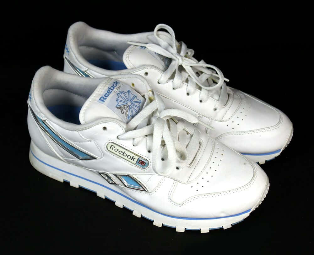 以彪馬鞋履與服飾展現個人風格 壁紙 — 一對白色Reebok Classic運動鞋，帶有藍色點綴和銀色條紋，放在黑色背景上。