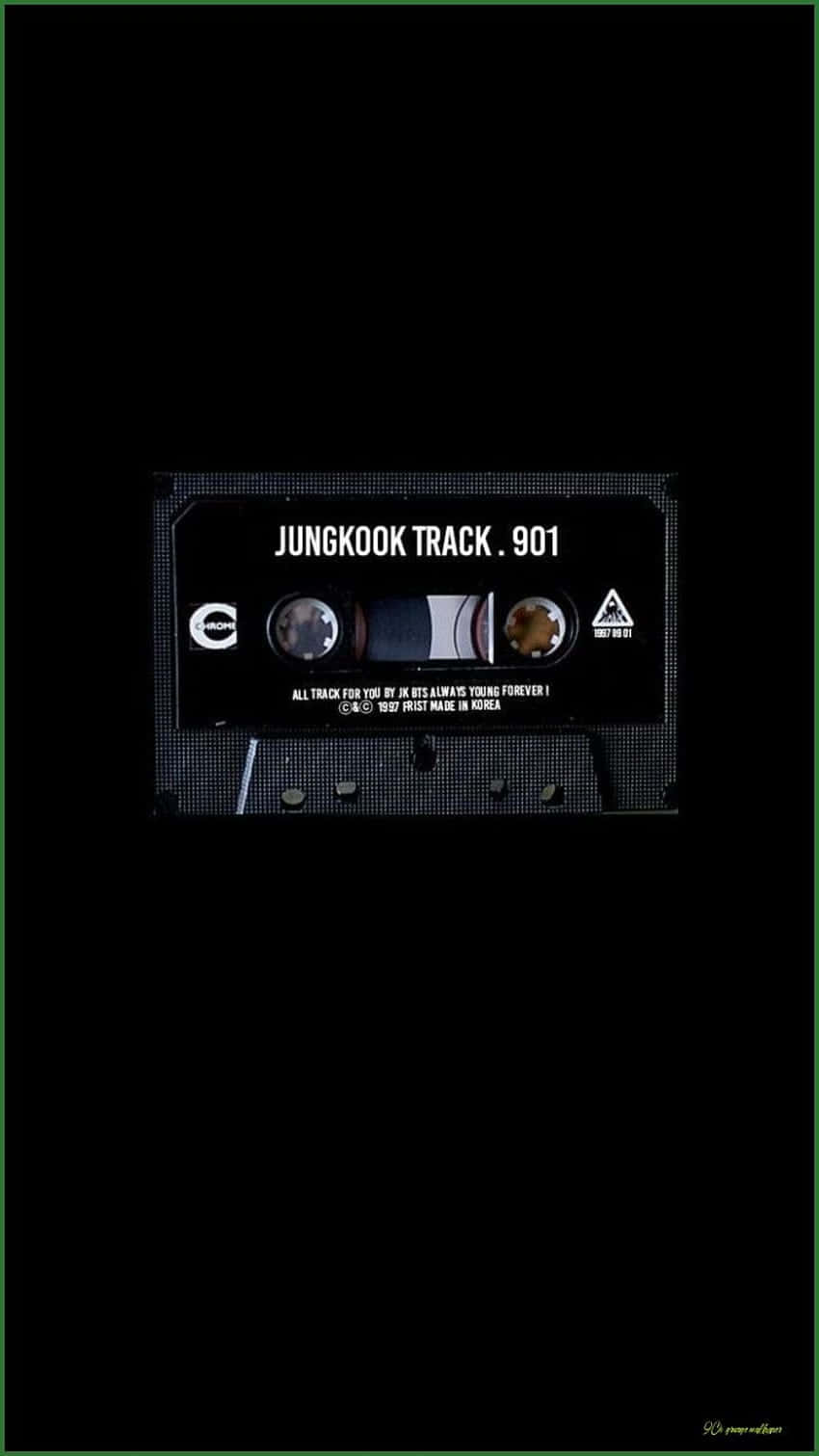 以復古風與現代感重現九十年代 壁紙 — 一盒標有 'JUNGKOOK TRACK . 901' 的復古卡式錄音帶，在漆黑背景上隱約發光。