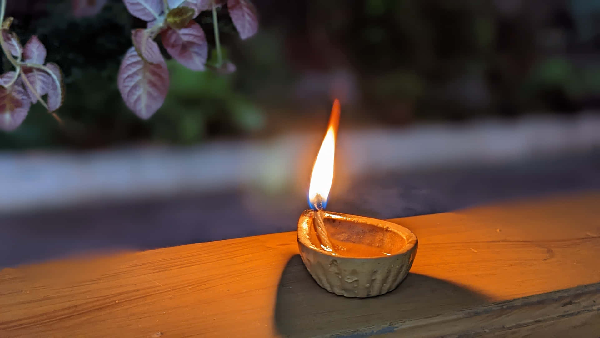 一個小油燈在紫色葉子附近的木質表面上明亮地燃燒。
