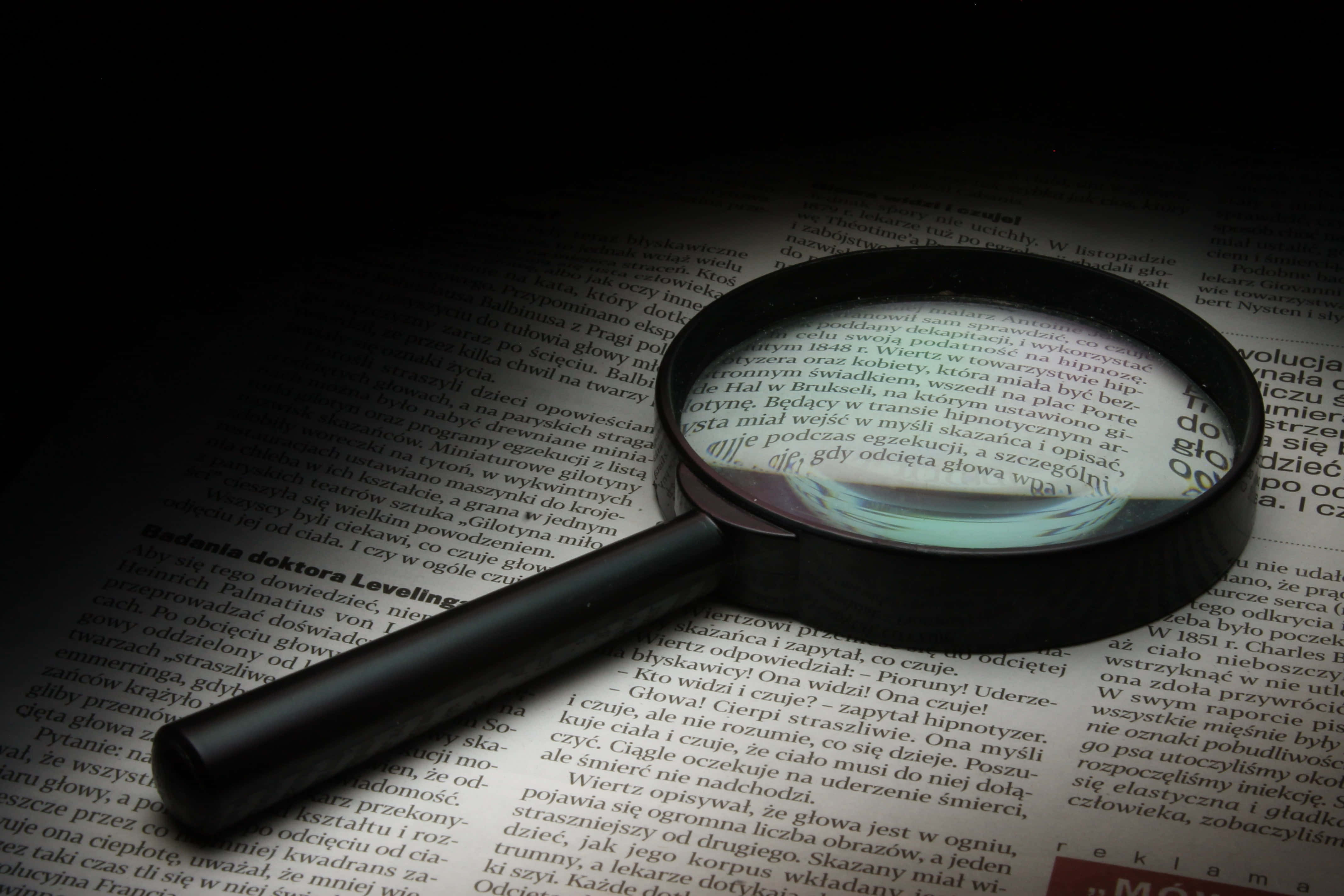 以放大鏡揭開秘密 壁紙 — 放大鏡放在一頁密密麻麻的波蘭文文字上，揭示印刷文字的近距離細節。