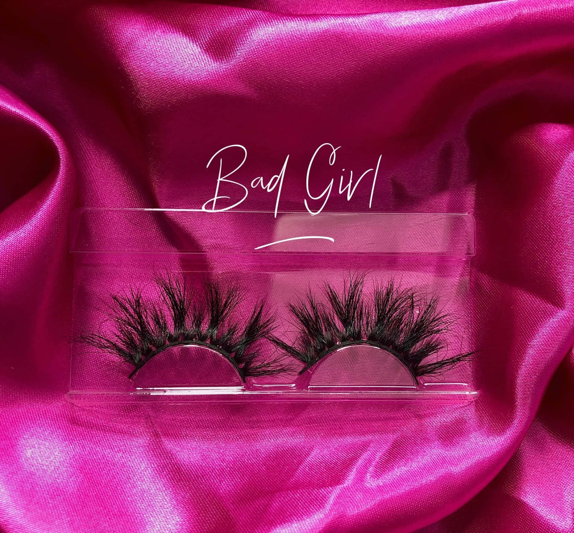 透明盒中的黑色假睫毛，置於粉紅色緞面上，帶有「Bad Girl」文字。