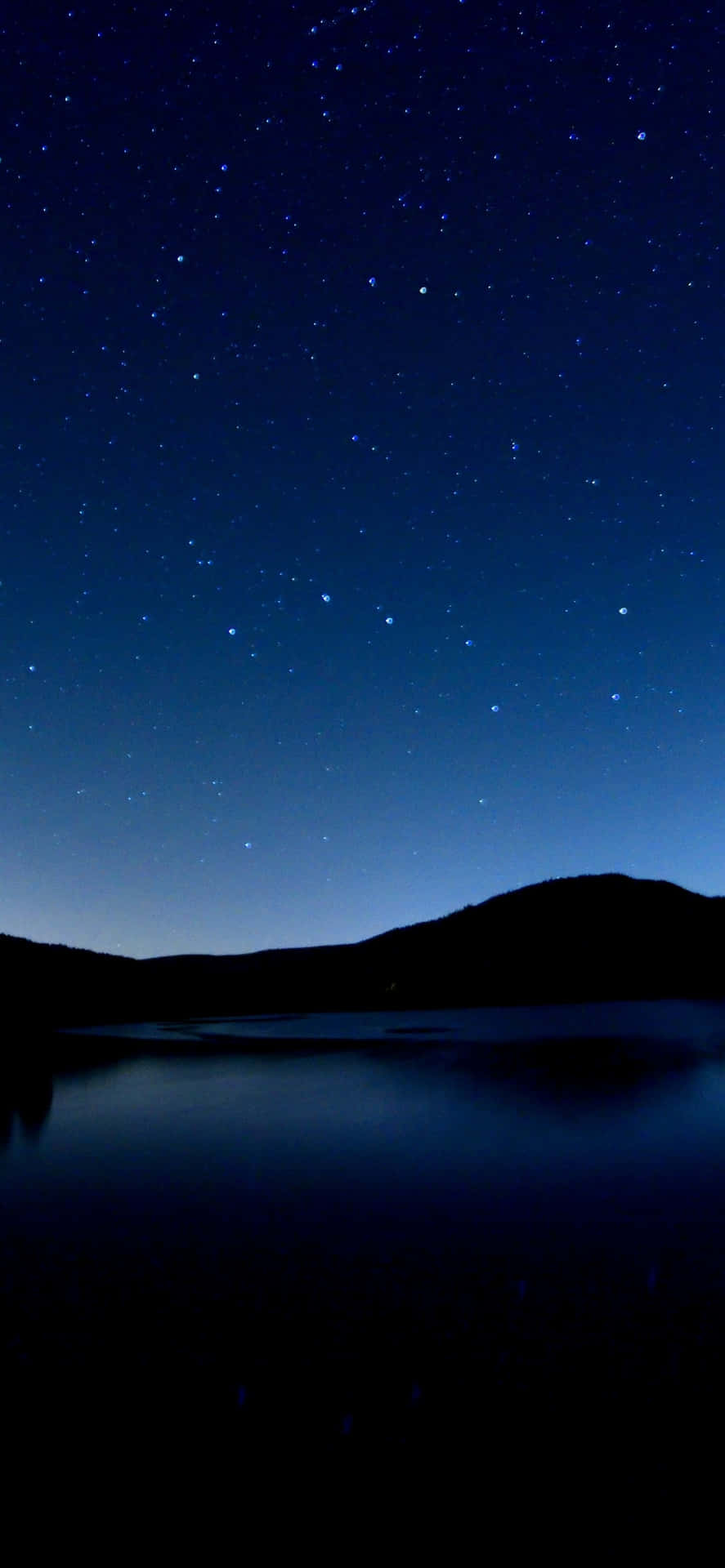 星空夜空映照在平靜的湖面，有黑暗的山丘