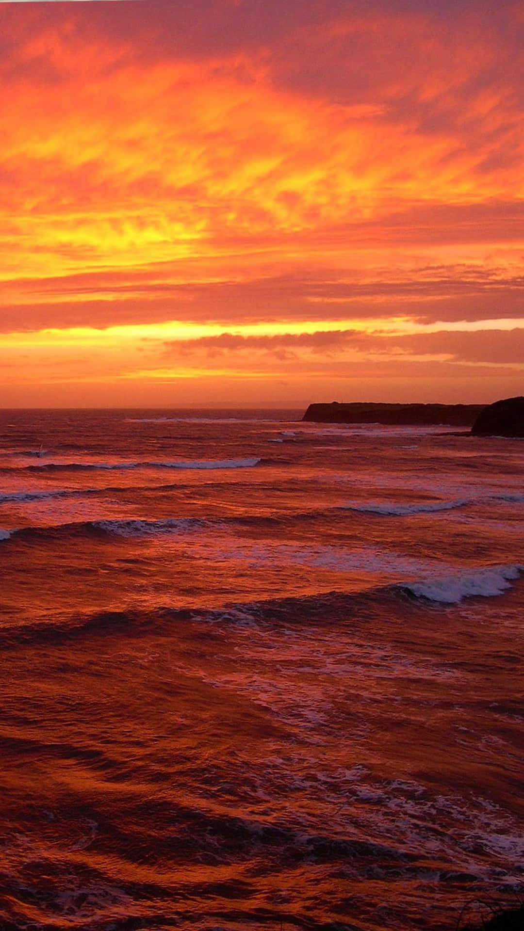 海浪和遠方懸崖上充滿活力的橙紅色夕陽
