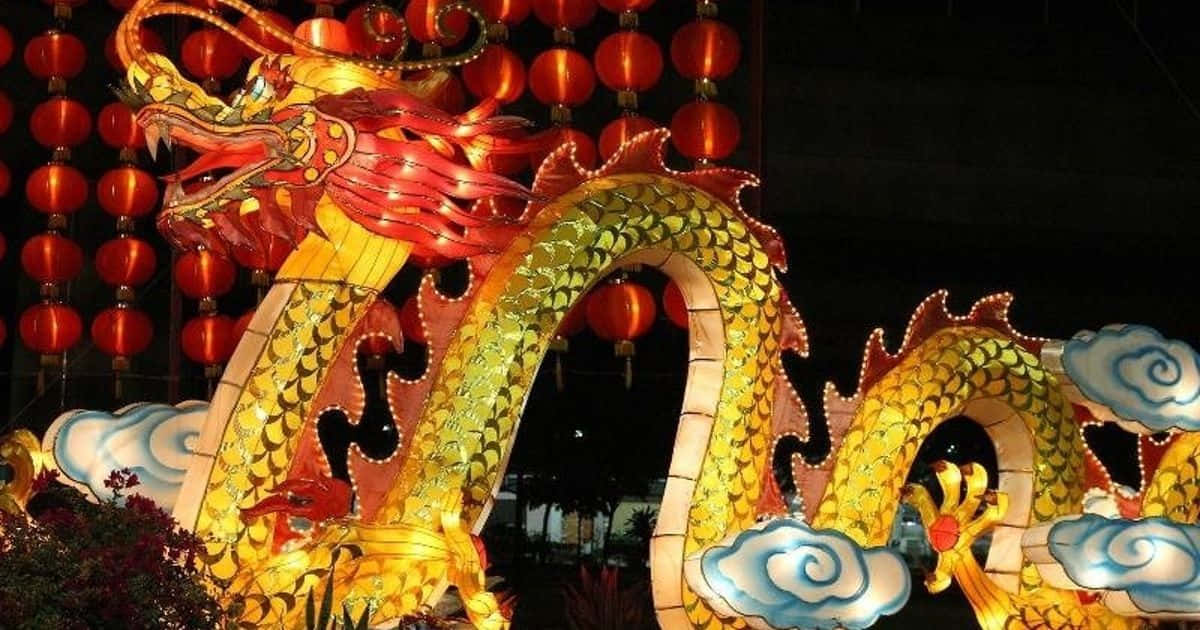 以時尚裝飾慶祝中國新年 壁紙 — 一個發光的金色龍燈籠，帶有紅色點綴，在懸掛的紅色燈籠中盤繞，背景是黑暗的夜空。