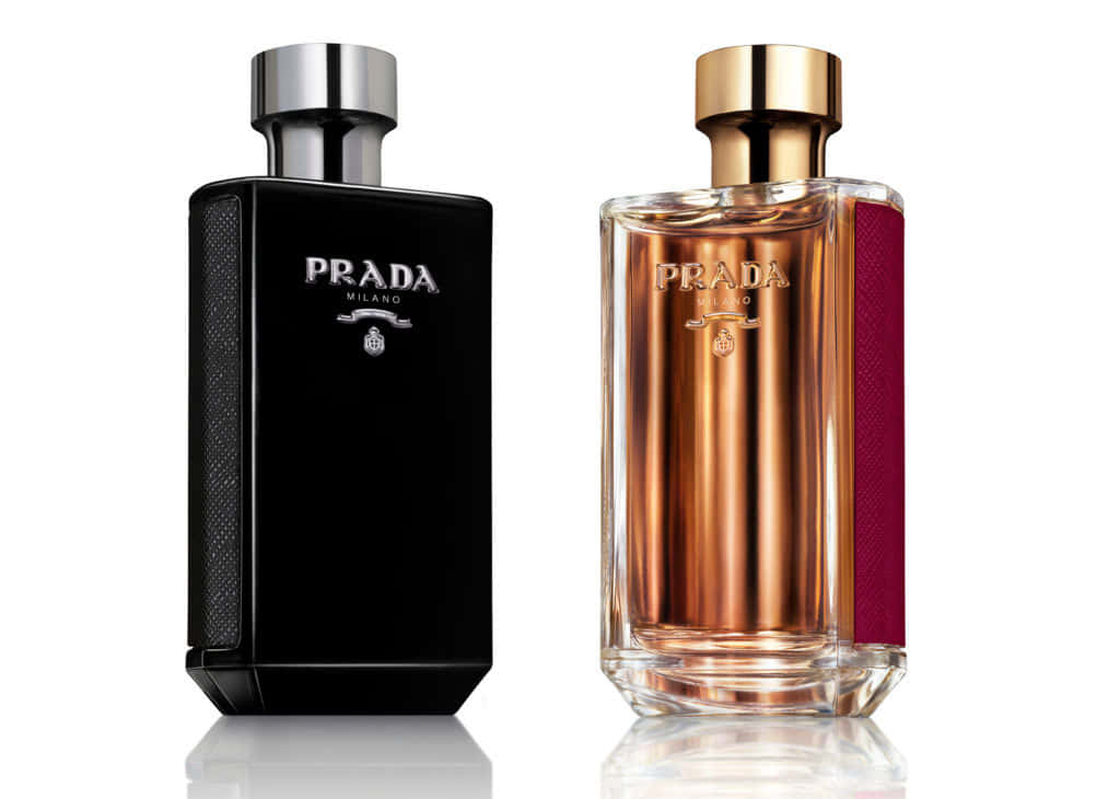 「以普拉達開啟奢華」 壁紙 — 兩瓶Prada Milano香水，一瓶黑色紋理，一瓶琥珀色玻璃帶酒紅色條紋，並排立在反光表面上。
