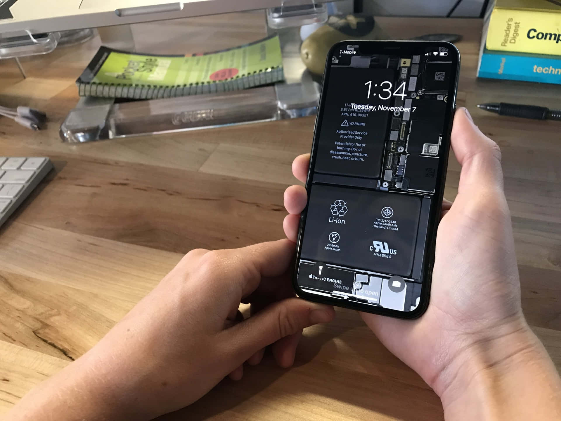 雙手拿著一部損壞的iPhone，在木桌上顯示內部零件。