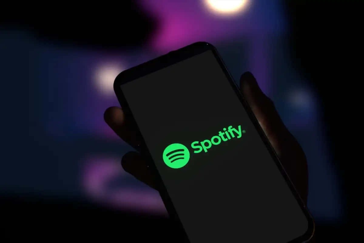 手拿手機，在夜間顯示綠色光中的Spotify應用程式標誌。