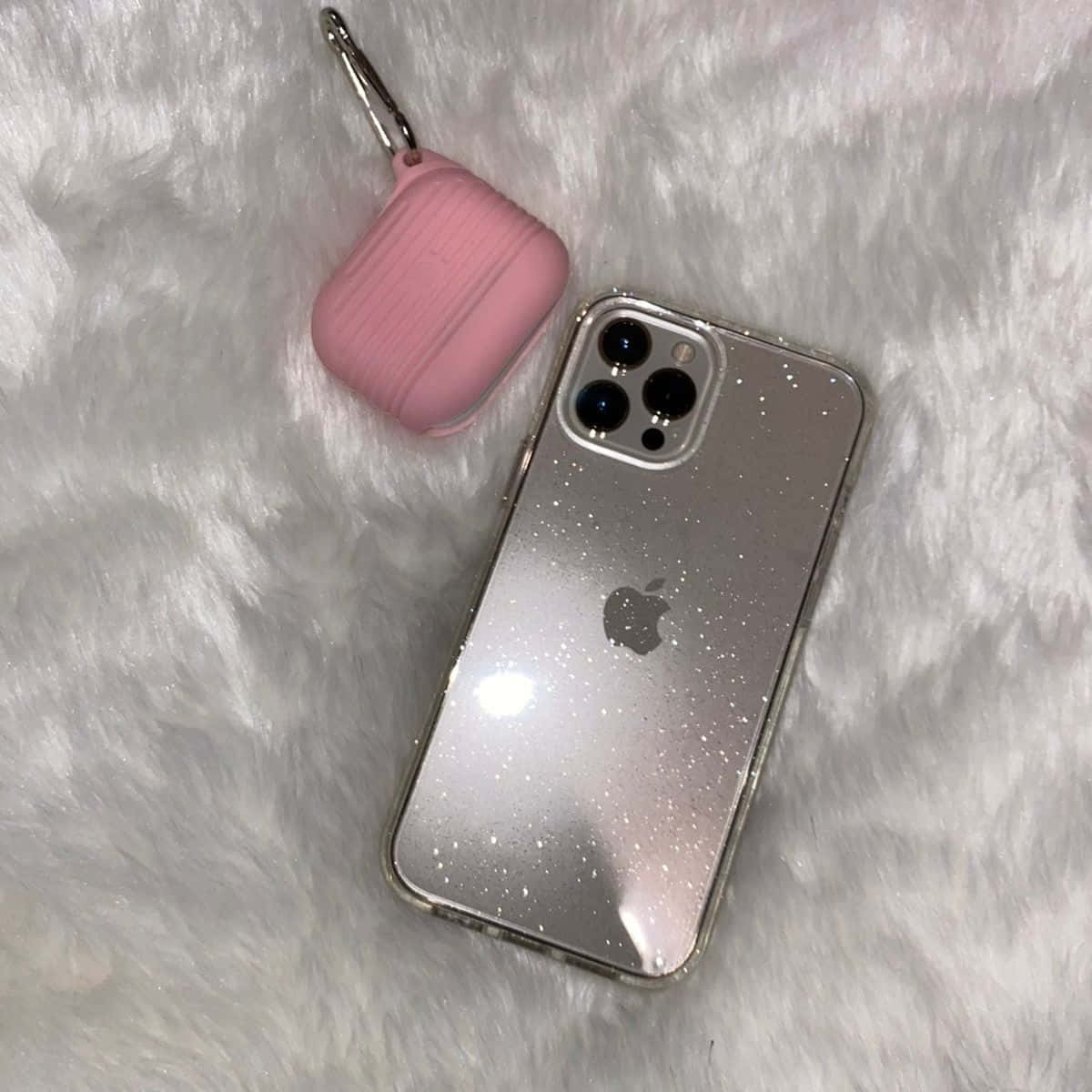 以最新酷炫科技迎接 iPhone 12 壁紙 — 一部銀色閃粉iPhone和粉紅色AirPods保護殼放在毛絨白色紋理表面上。