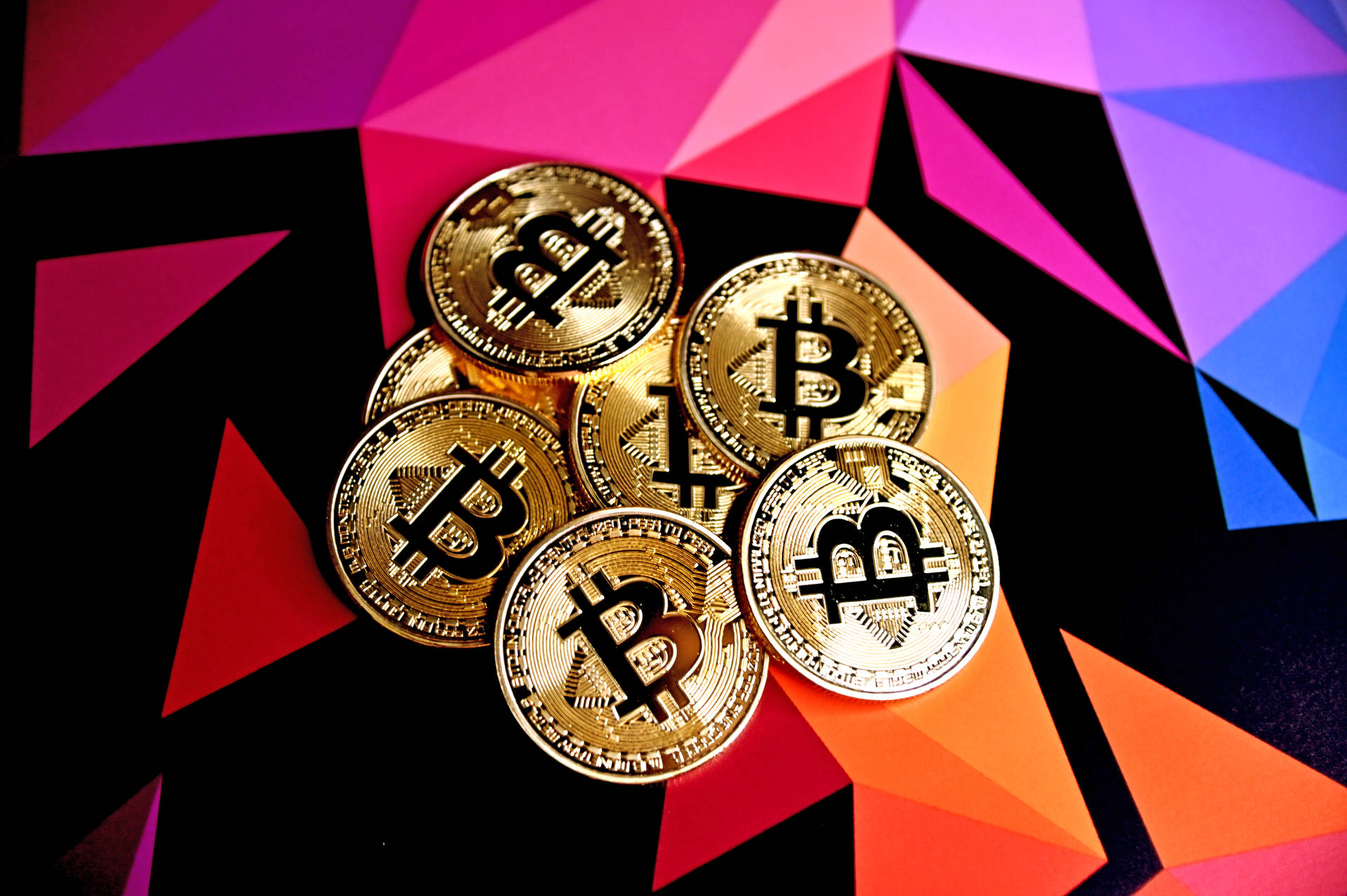 在彩色幾何圖案背景上的一堆金色比特幣硬幣。