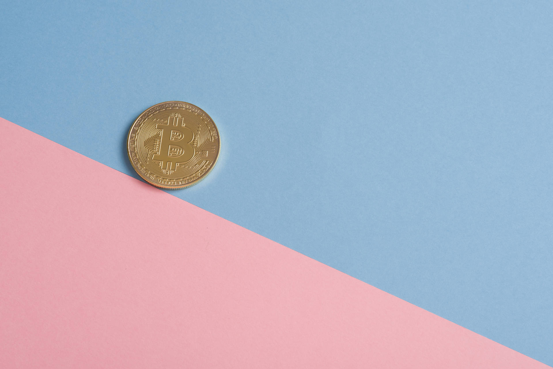 金色比特幣硬幣在粉紅色和藍色背景上。