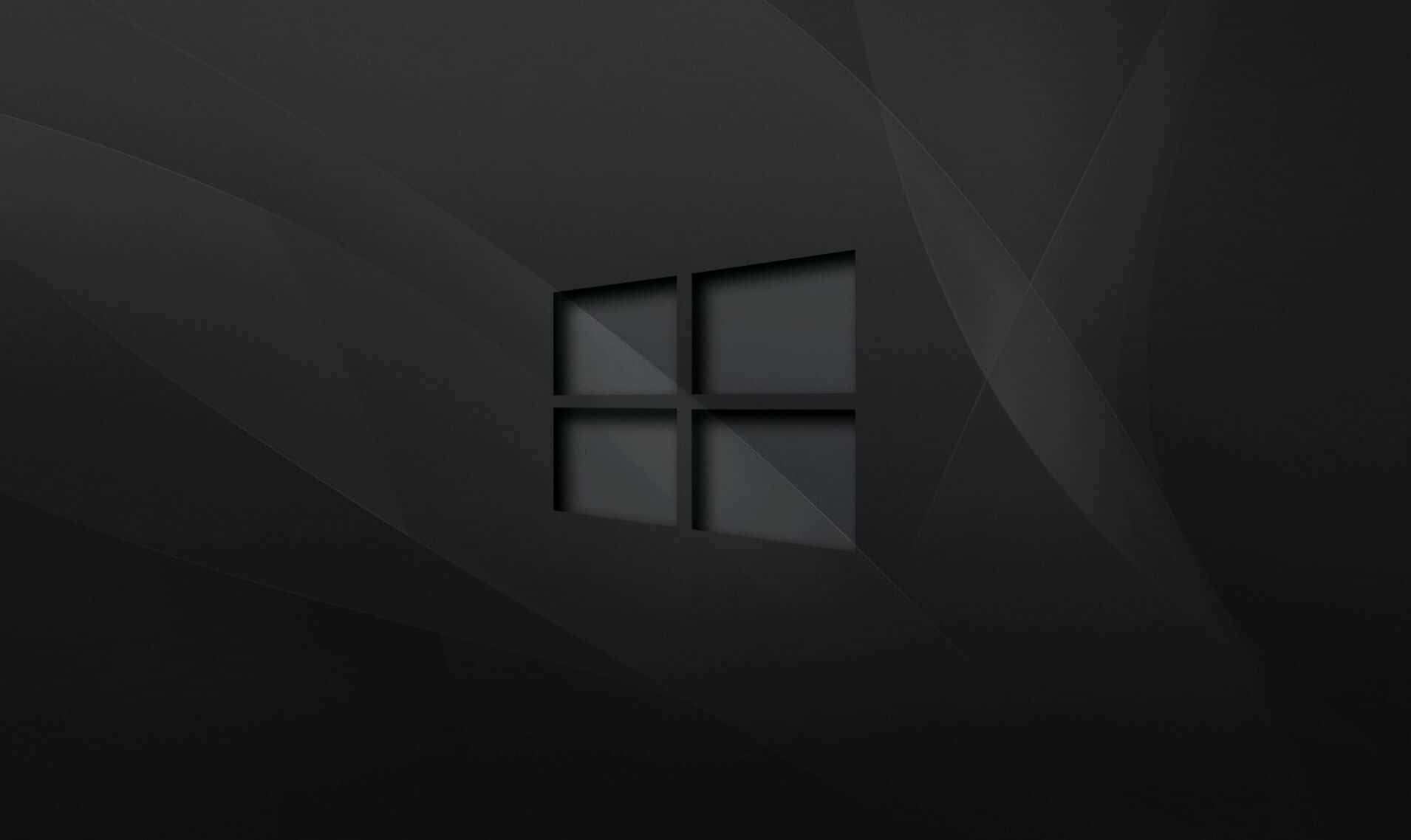 以活力桌面背景體驗 Windows 10 壁紙 — 一個極簡風格的深灰色抽象背景，中央有一個微妙的浮雕Windows標誌，位於柔和的幾何摺痕中。