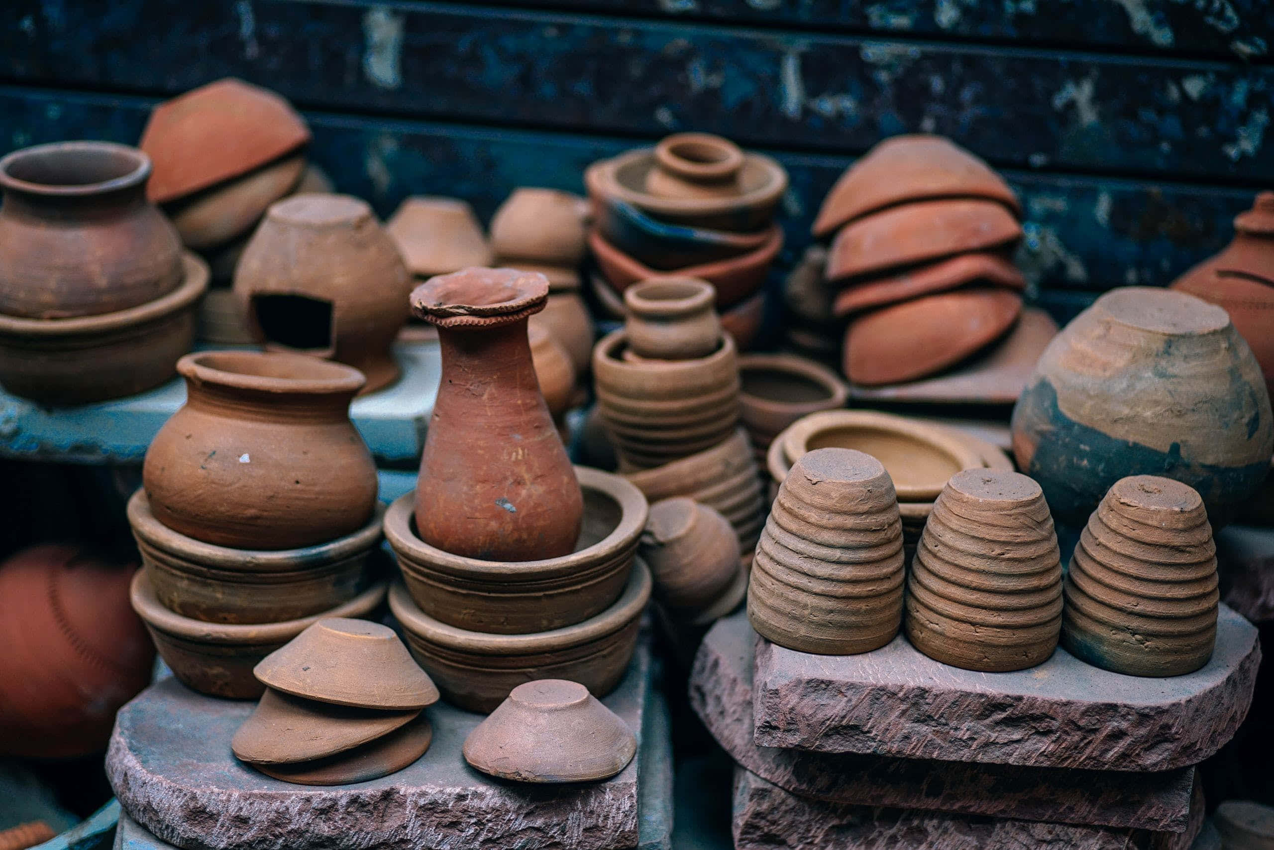 Ceramics 桌布 壁紙 — 以溫暖大地色調堆疊的赤陶鍋和碗，放置在石板上，背景是風化的藍色牆壁。