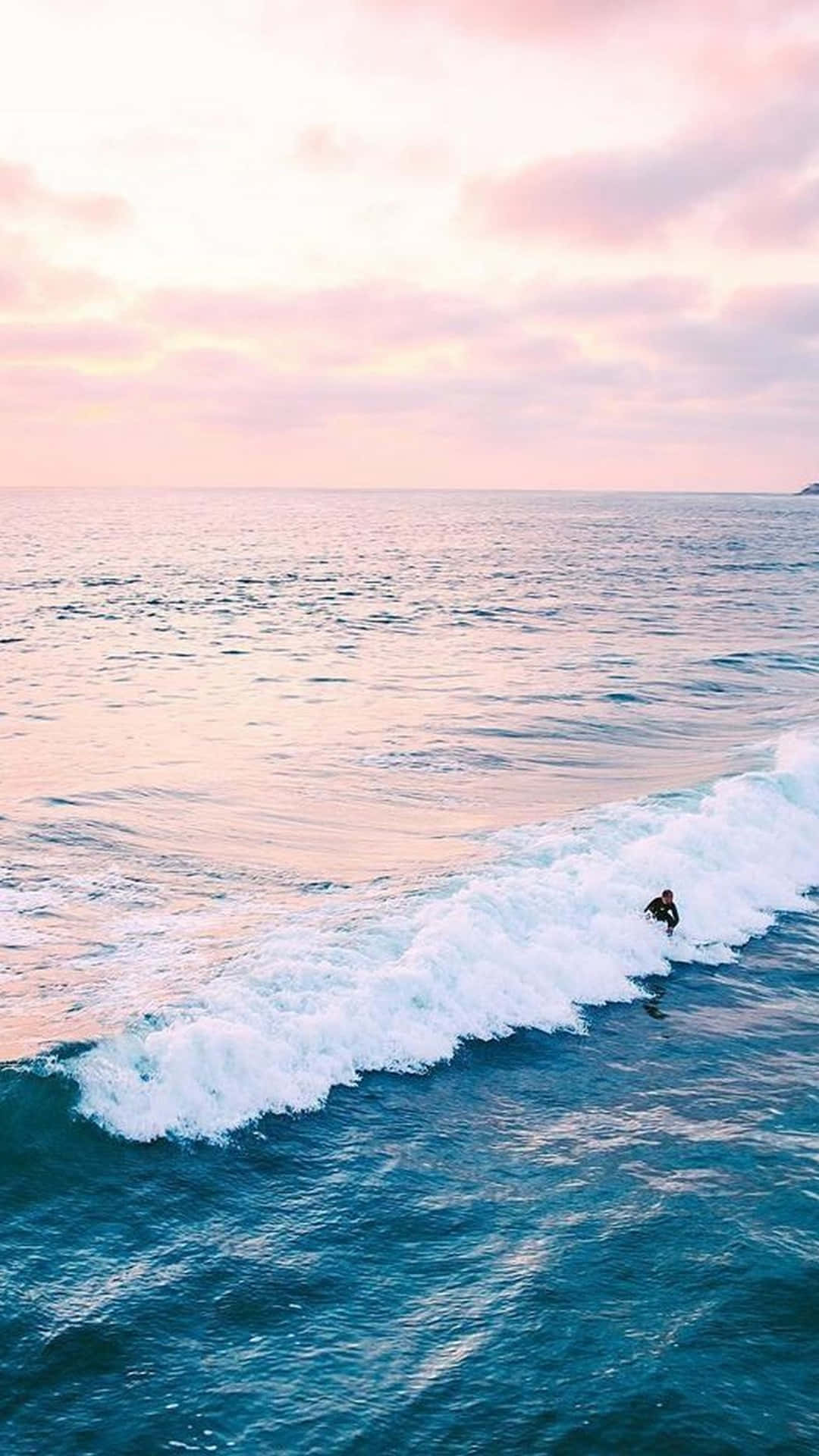 衝浪者在日落時分在粉紅和藍色海洋色調的海浪上滑行。