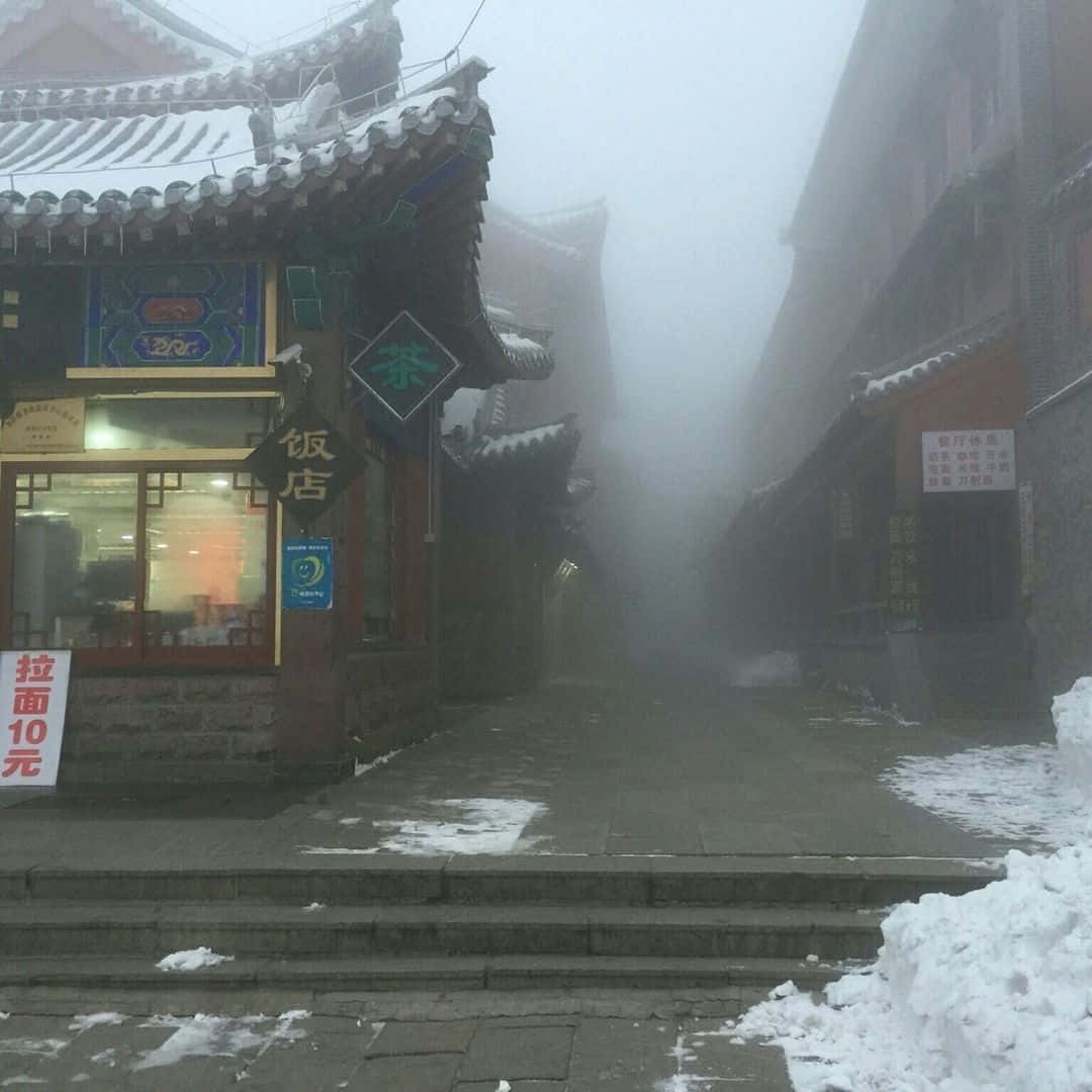 以灰色美學打造理想工作空間 壁紙 — 一條有雪有霧的小巷，位於傳統中國小鎮，屋頂覆蓋白雪，商店招牌閃爍發光。