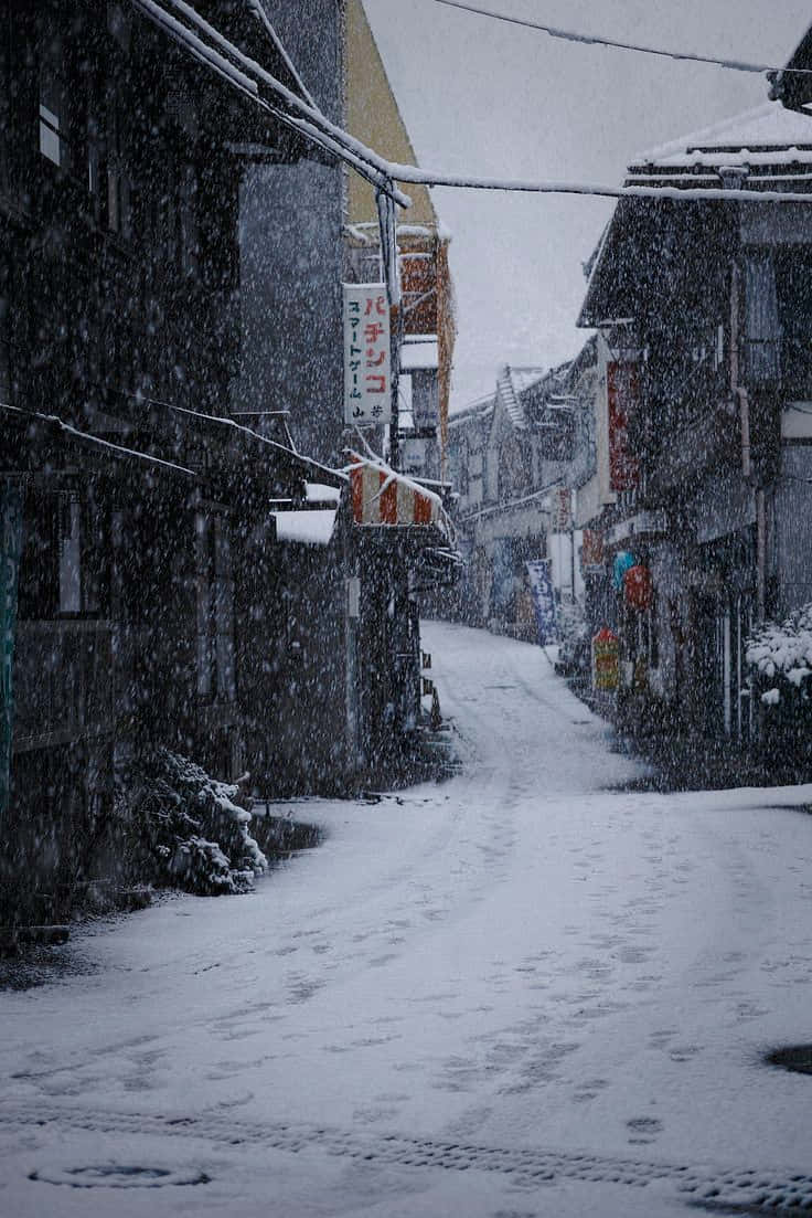 「以灰階生活」 壁紙 — 白雪覆蓋著一條寧靜的日本街道，雪花在傳統建築之間昏暗陰沉的光線中飄舞。