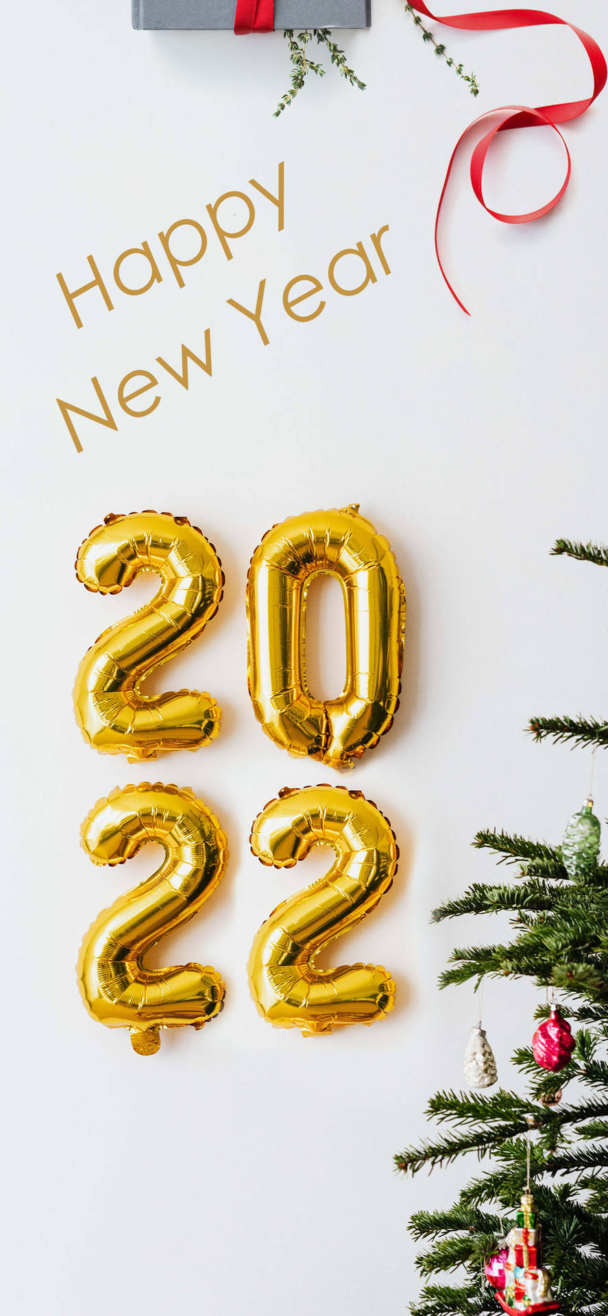 金色2022氣球旁邊有聖誕樹，樹上掛有裝飾品和禮物盒。