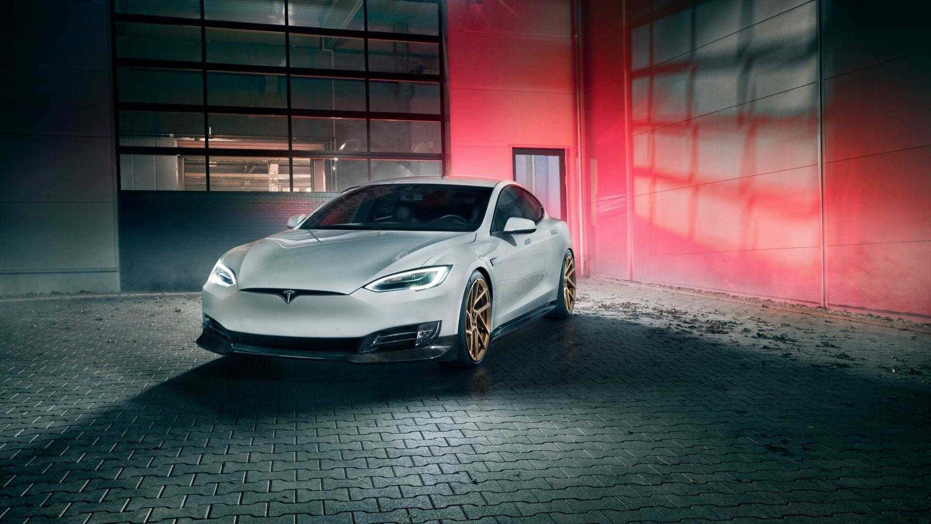 以特斯拉標誌性設計提升效率與風格 壁紙 — 一輛時尚的銀色Tesla Model S配金色輪圈，停在鵝卵石地面上，上方有戲劇性的紅色牆壁照明。