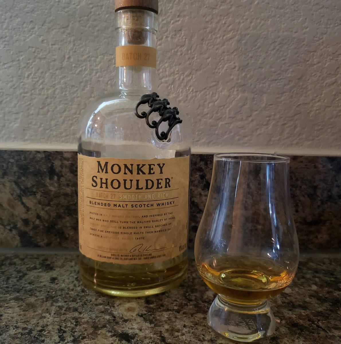 Monkey Shoulder威士忌瓶和杯在花崗岩枱面上。