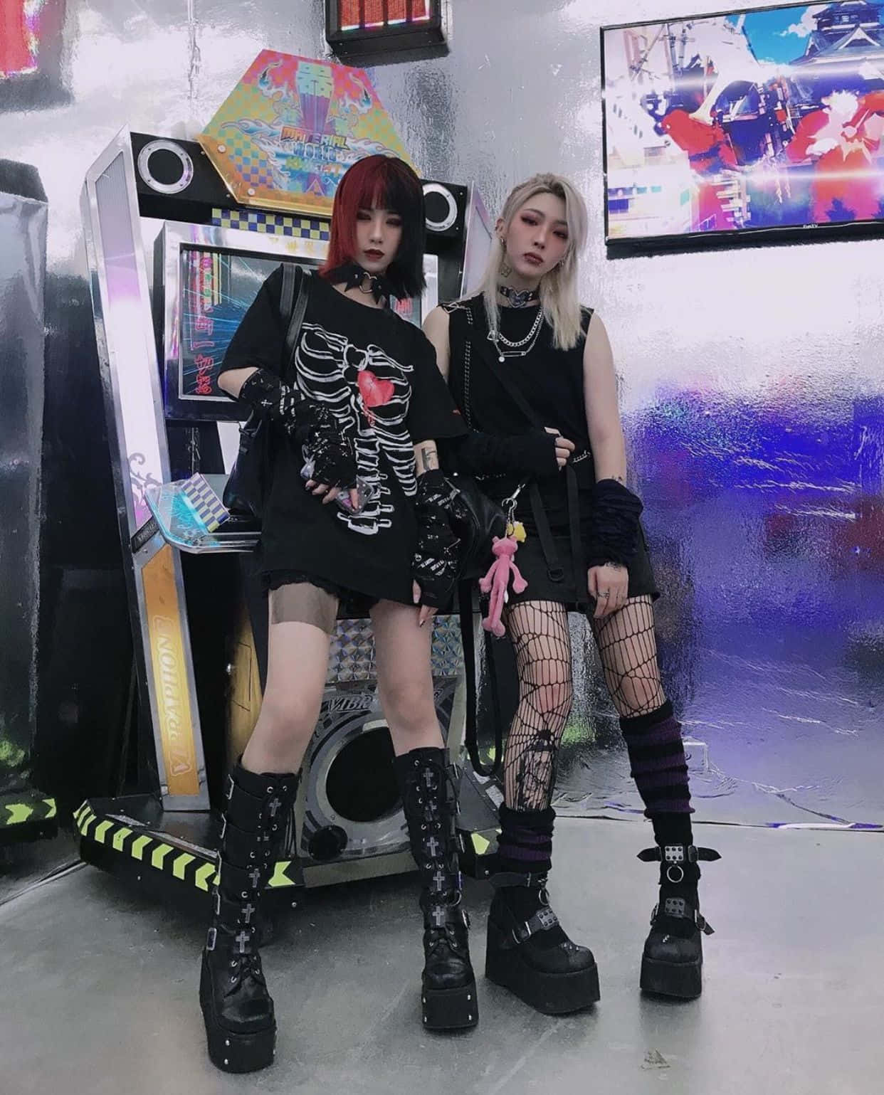 兩位哥德龐克少女穿著黑色服裝，在霓虹遊戲室中靠近街機擺姿勢。