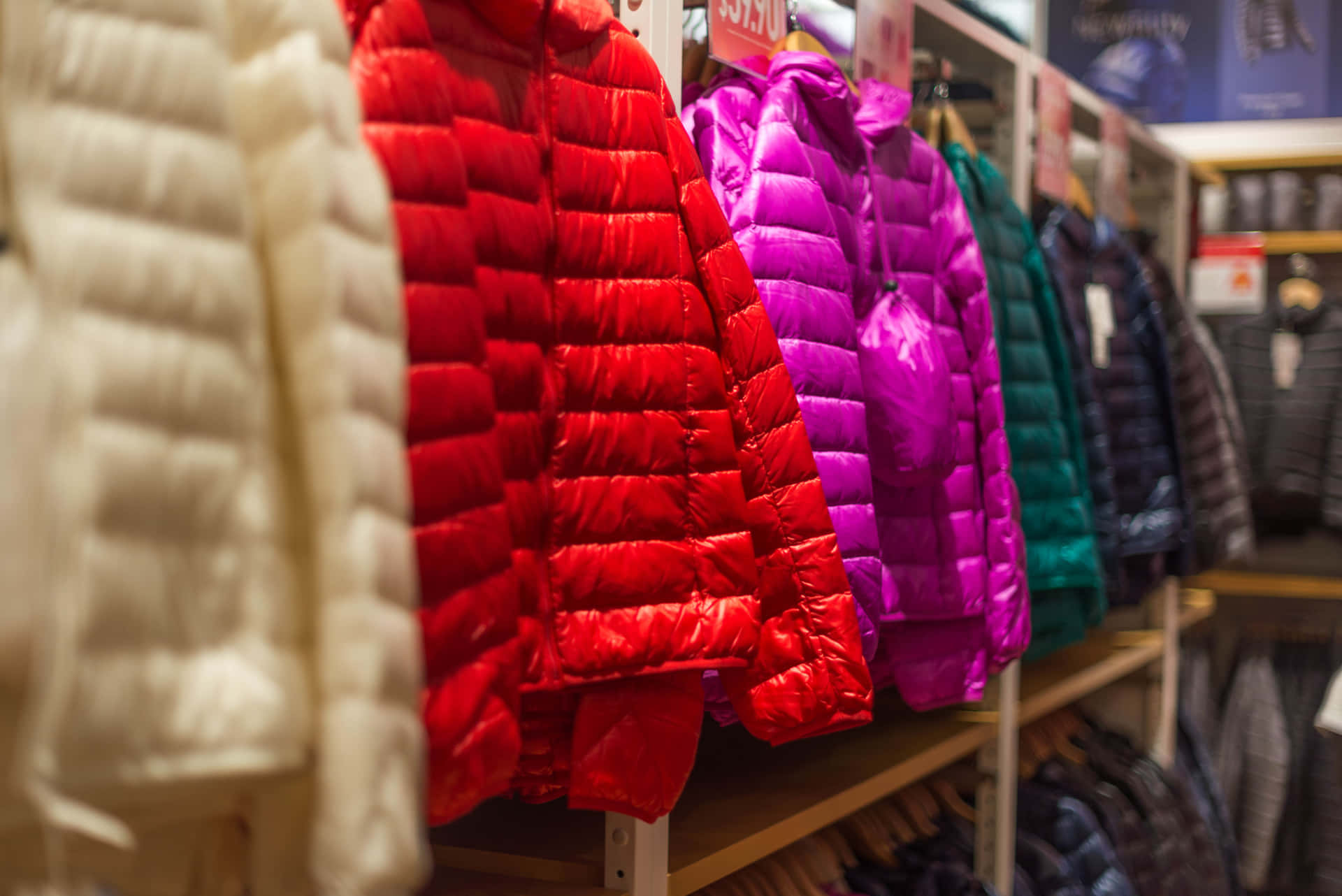 一排色彩繽紛的絎縫外套掛在服裝店的展示架上。