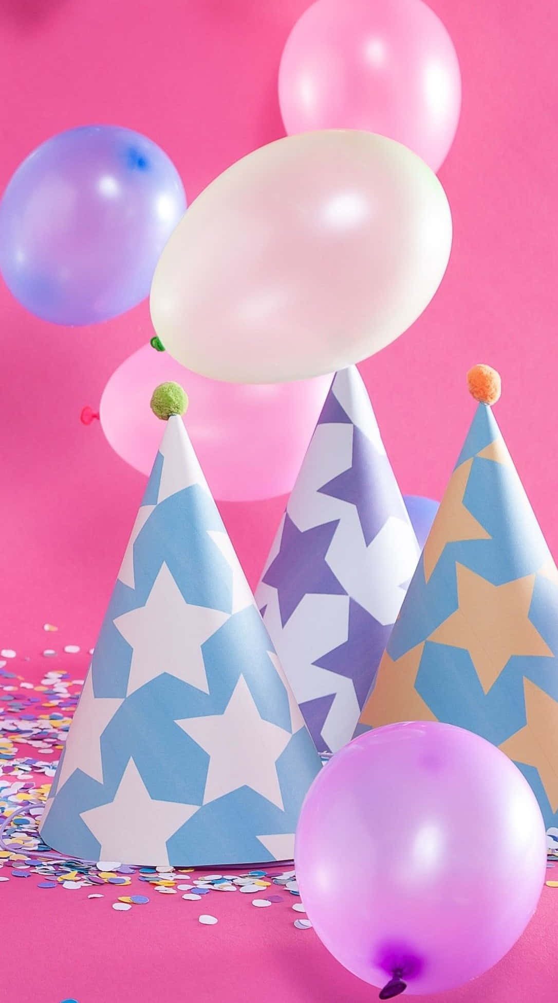 以粉紅生日慶祝重要時刻 壁紙 — 粉彩氣球和星星圖案的派對帽在充滿活力的粉紅色背景上，伴隨著五彩紙屑漂浮。